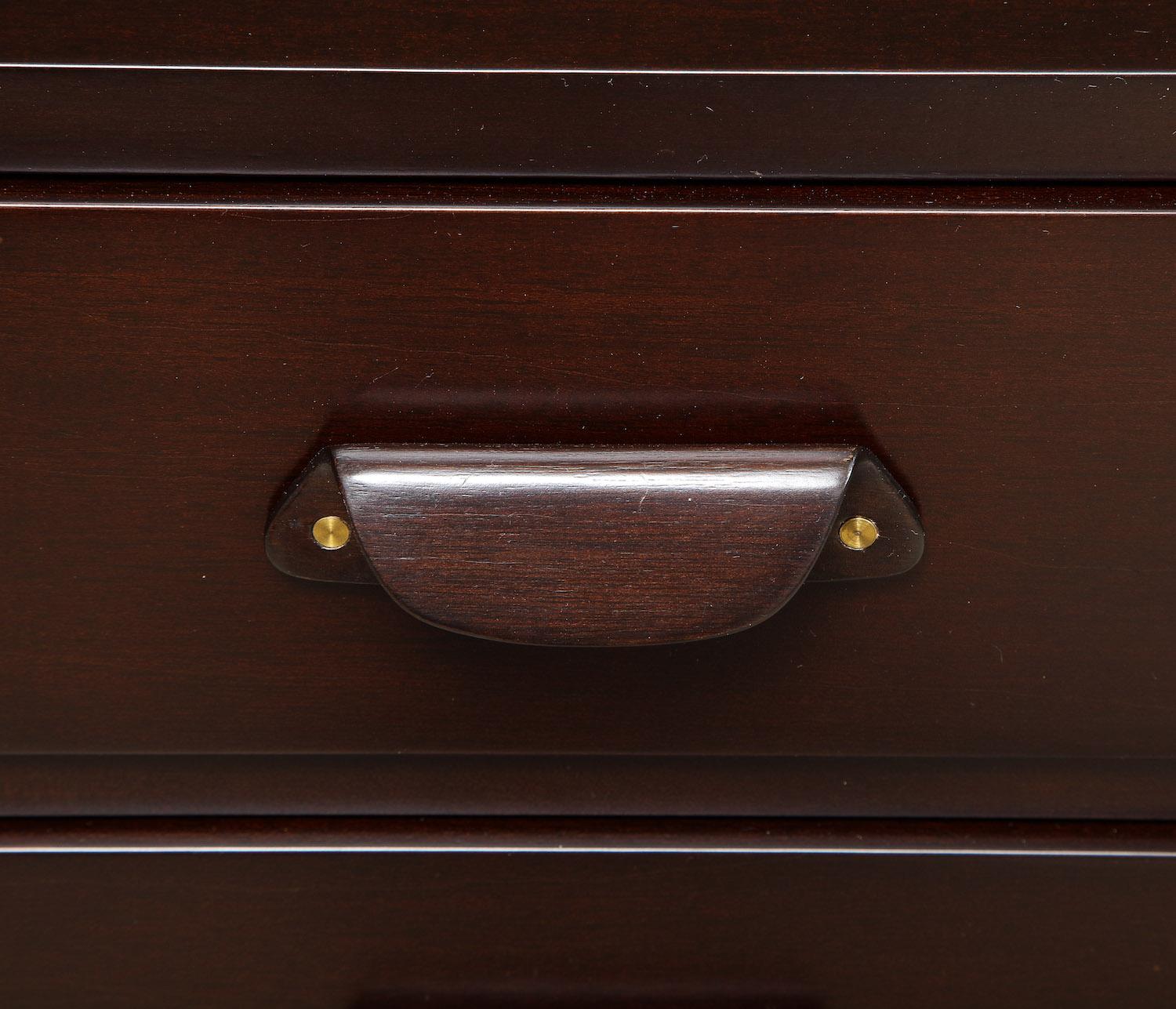 Dark stained wood with sculptural wood handles. Pair of 3-drawer mini chests that make great bedside tables. Green Dunbar label affixed to interior of top drawer in each cabinet. Wood has been recently refinished.