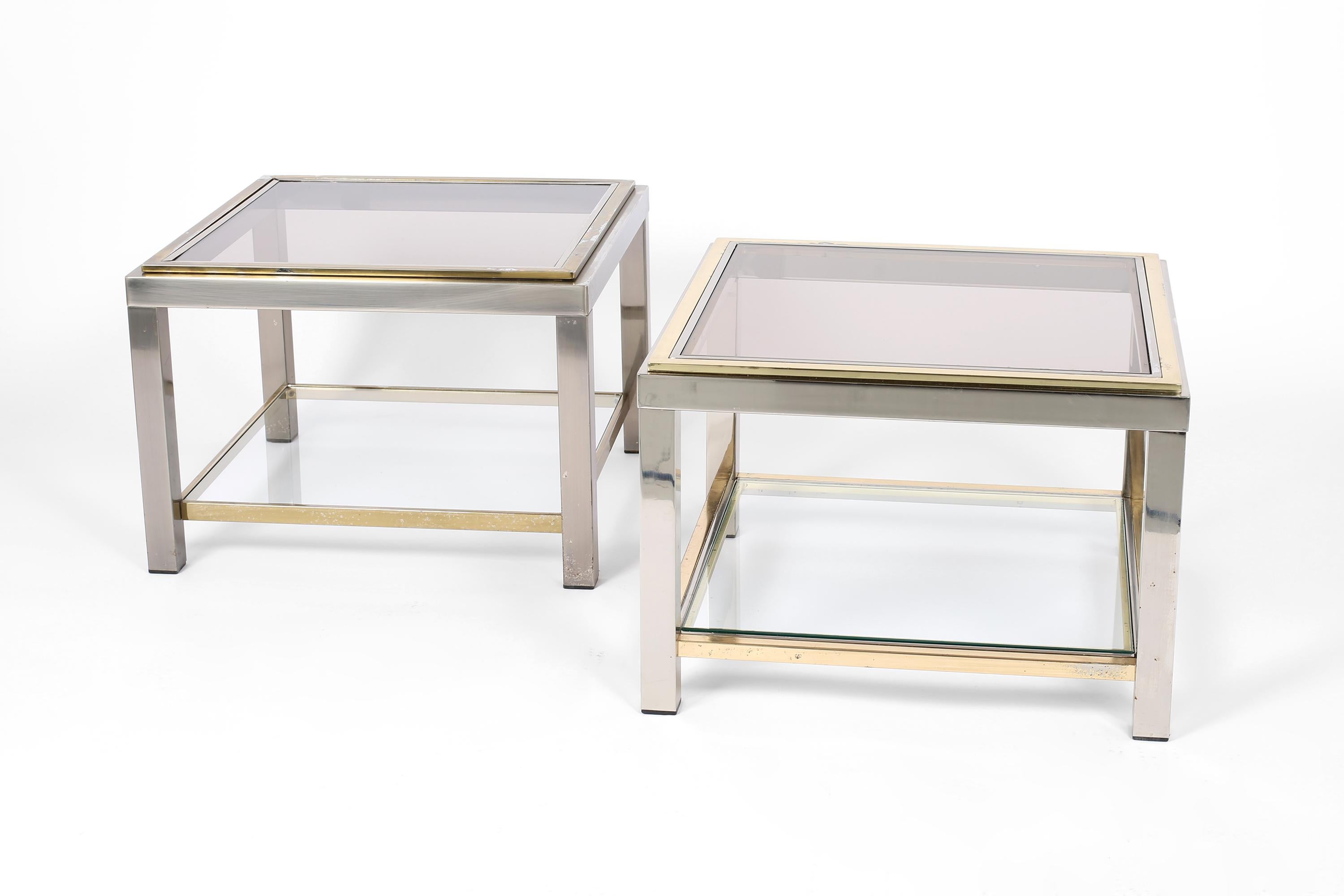 A near pair of side tables in polished and gilt steel, with smoked glass tops and a useful clear glass lower tier. In the manner of Jean Charles or Guy Lefevre. French, c. 1970s.