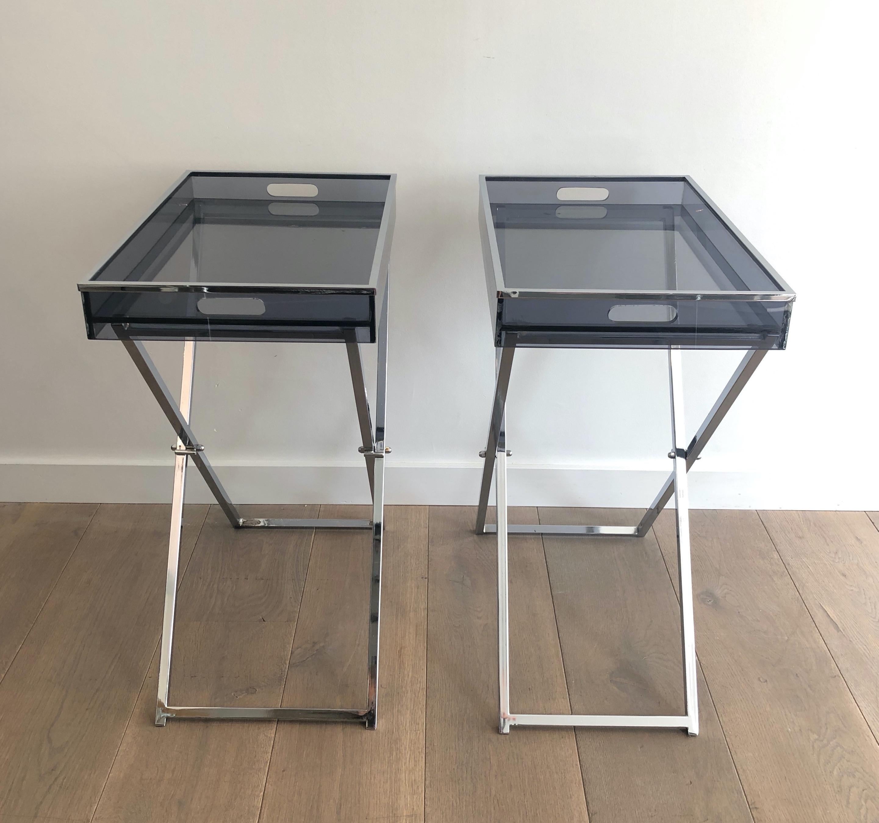 This pair of side tables is made of folding chrome bases with blueish lucite tops. This is a French work. Circa 1970.