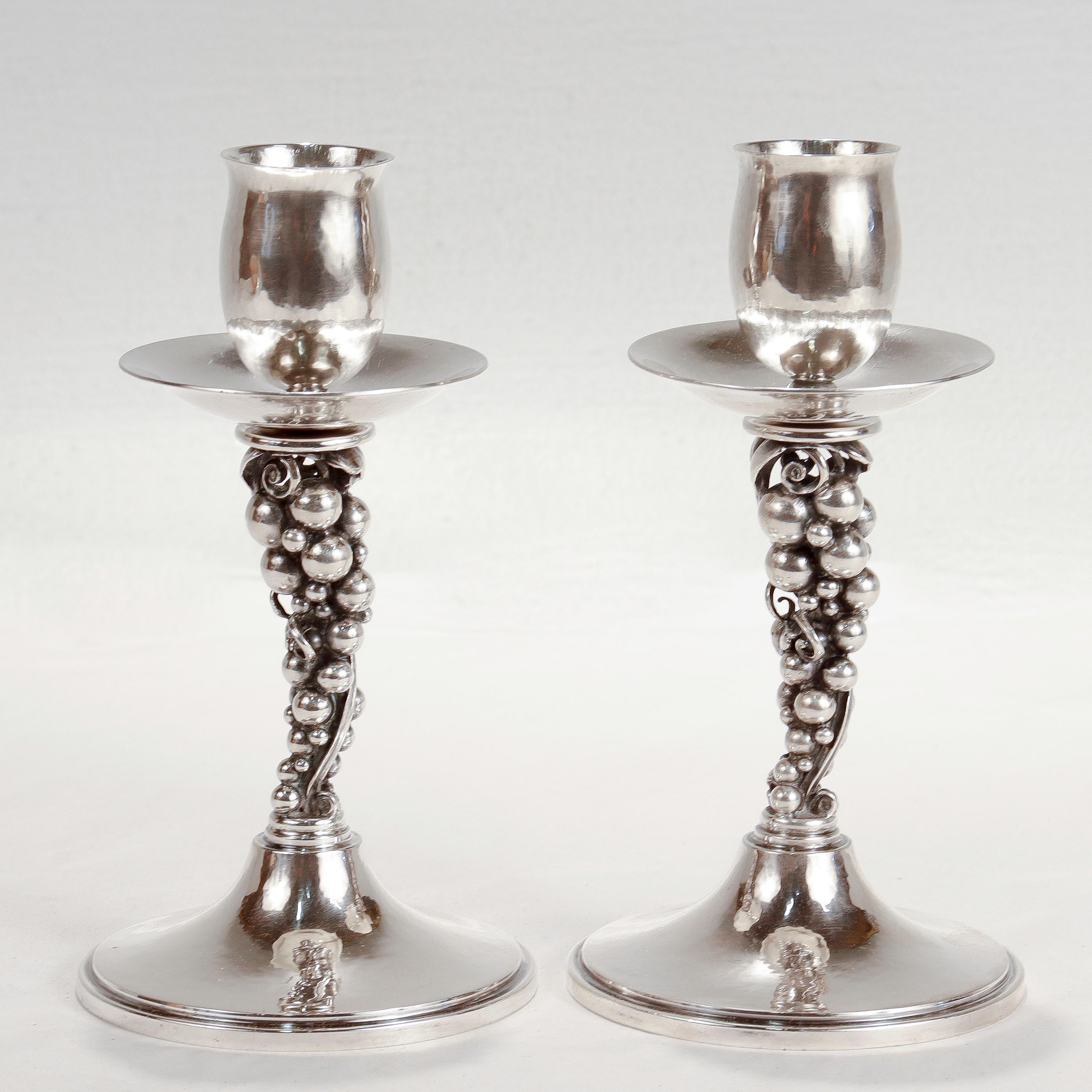 A fine pair of Danish Modern sterling silver candlesticks.

By Aage Weimar of Copenhagen, Denmark (active 1937 - 1966).

In the Jensen style.

With grape cluster pedestals on hand hammered bases supporting tulip shaped candlecups & hand hammered