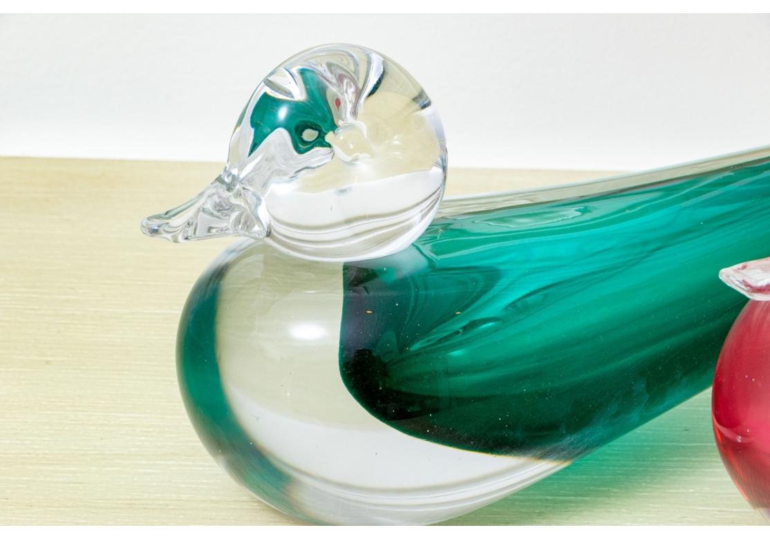 A pair of Murano Glass Duck Sculptures with fine form and color. Signed on the bases. Both cased glass, one in turquoise and clear, the other in pink and clear. Wood duck shapes with holes in the ends of the raised tails as vases. 

Dimensions:L. 9