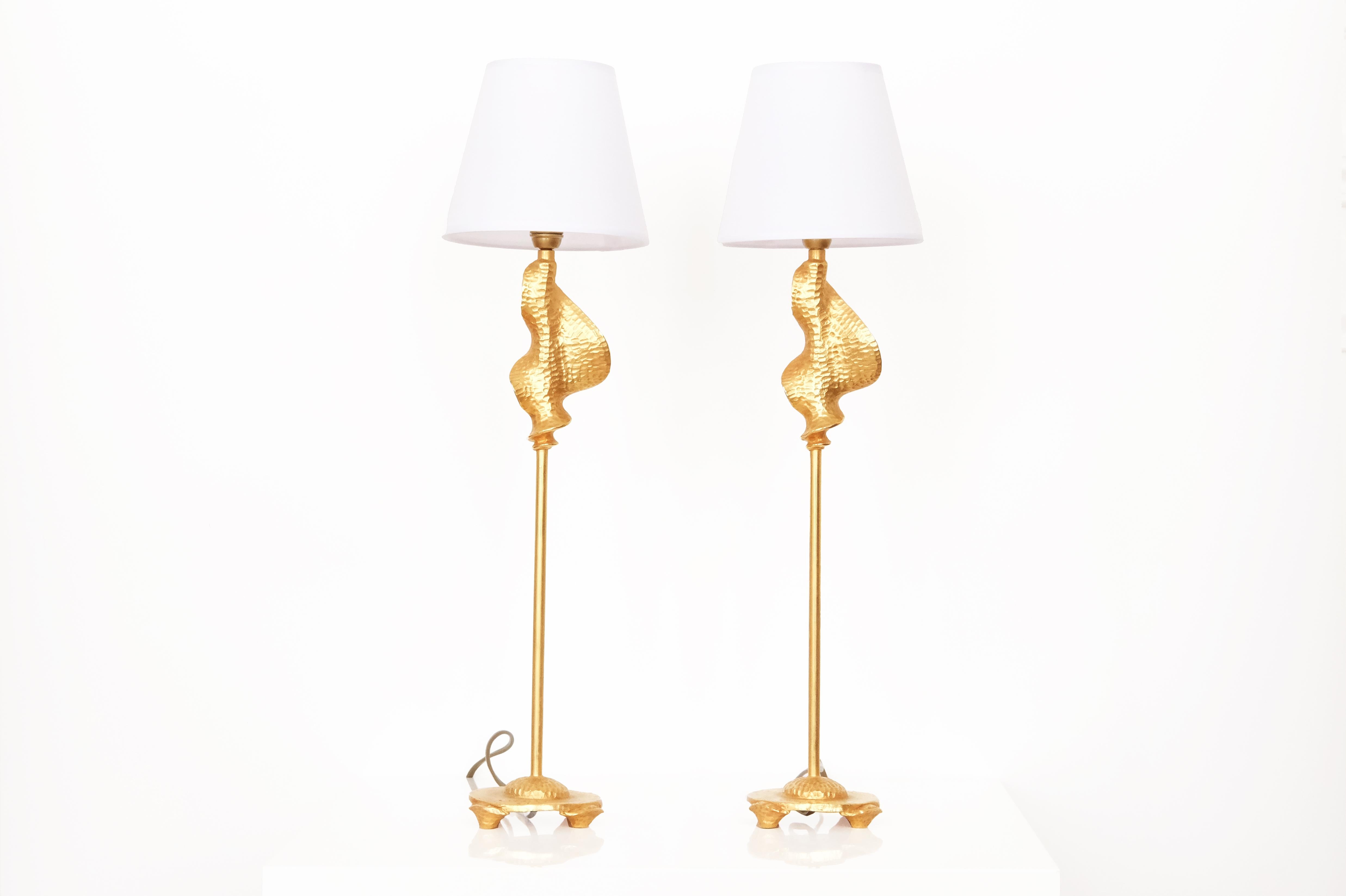 A sophisticated 20th century  pair of table lamps by Nicolas de Wael in gilt bronze, each signed on the base. Of refined proportions, the design features a slender shaft rising from a circular, textured base with delicately modeled feet. The central