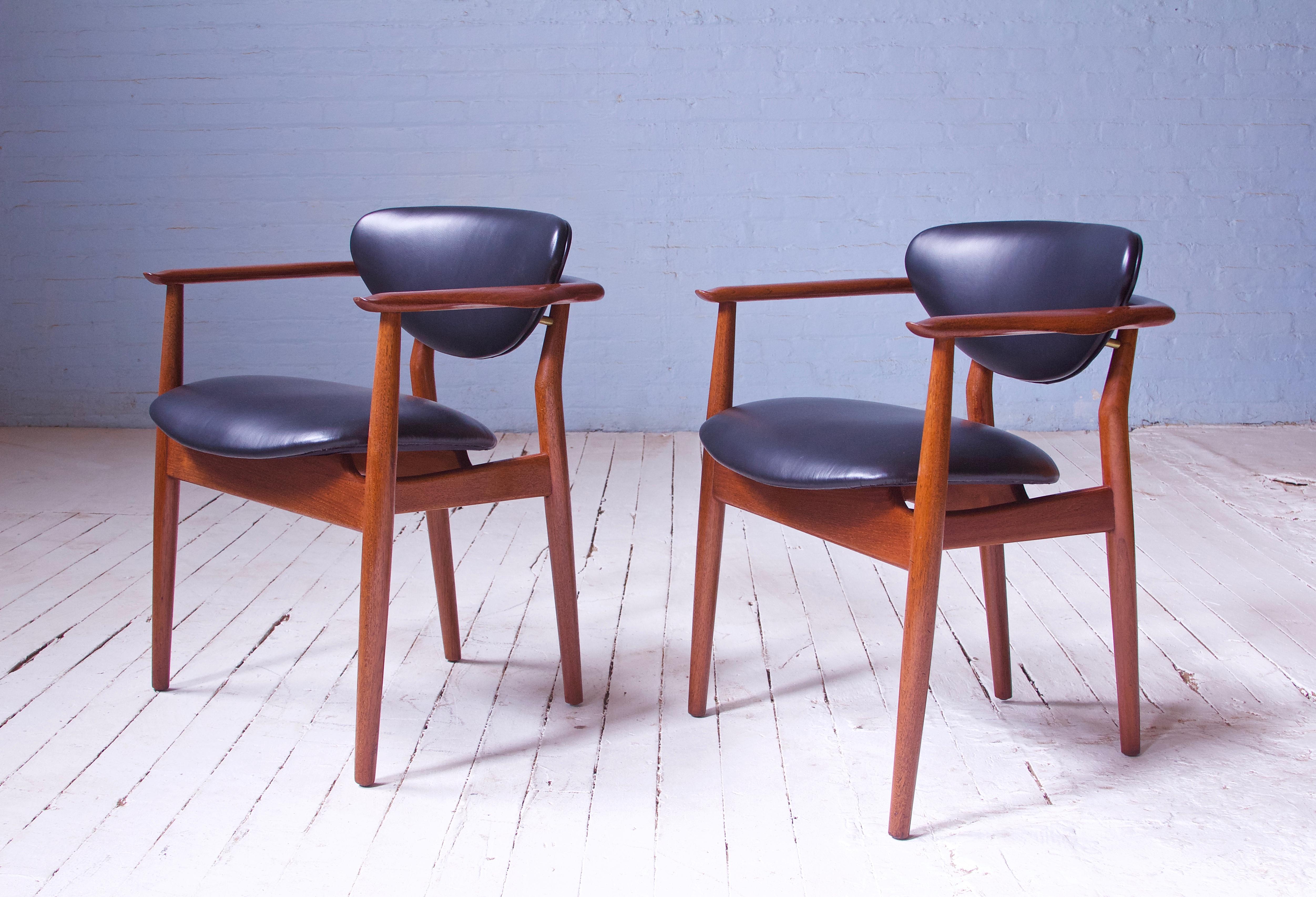 A very rare pair of vintage signed Finn Juhl for Niels Vodder (Cabinetmaker) 109 armchairs in teak, black leather, and brass. Elegantly suspended backrests supported by Finn Juhl's signature brass mounting hardware. Sculpted armrests are delicately