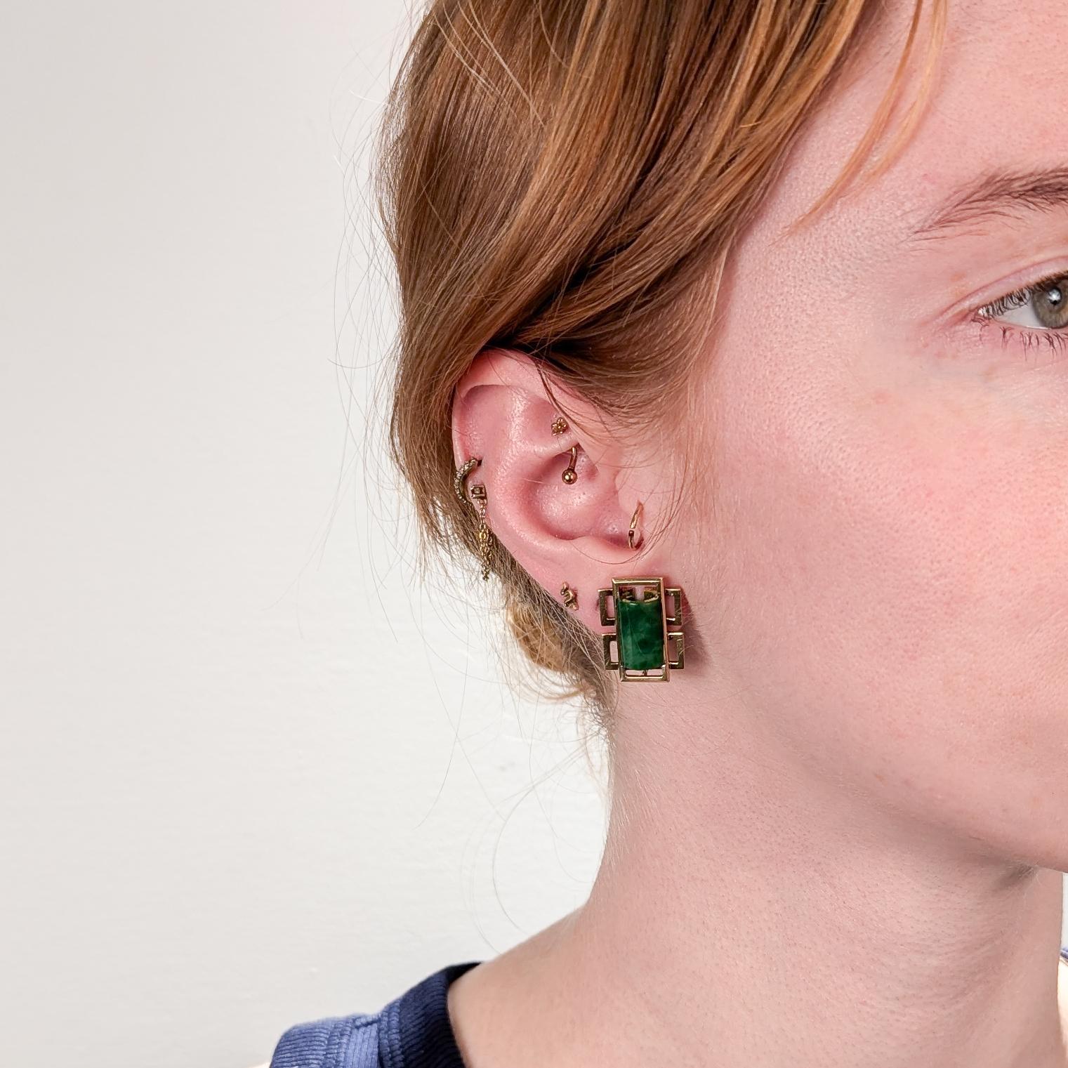 A fine pair of Mid-Century or Hollywood Regency clip-on earrings.

By Wedderien. 

In 18 karat yellow gold (with 14k white gold clips)

Each with a geometric form and a bezel-set semi-cylindrical green jadeite cabochons.

Marked Wedderien to the