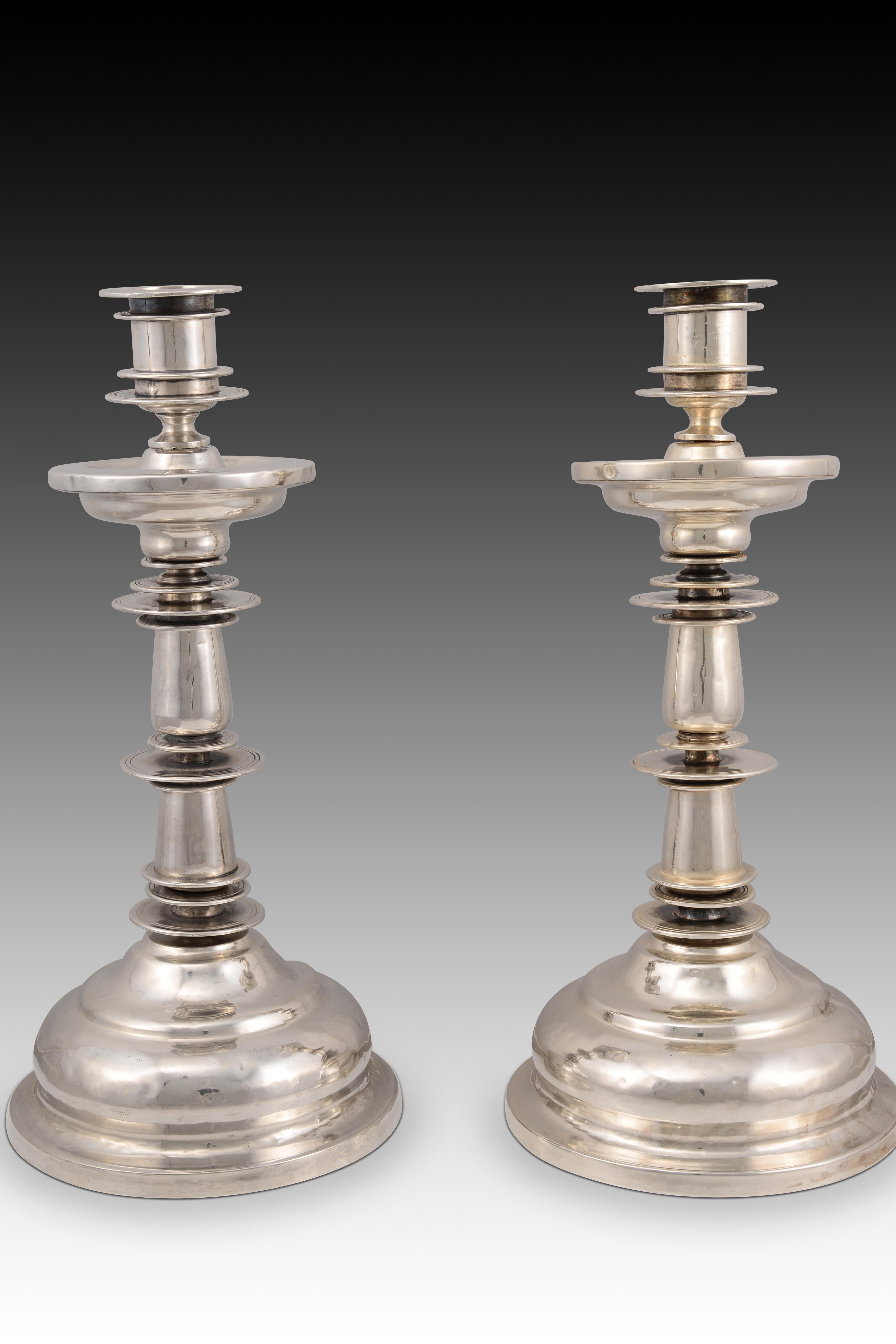 Pair of silver candlesticks. Century XVIII.
 Pair of candlesticks made of silver in an unadorned baroque style, with a clean and dynamic structure that expresses itself through the contrasting superposition of circular section elements. The lines
