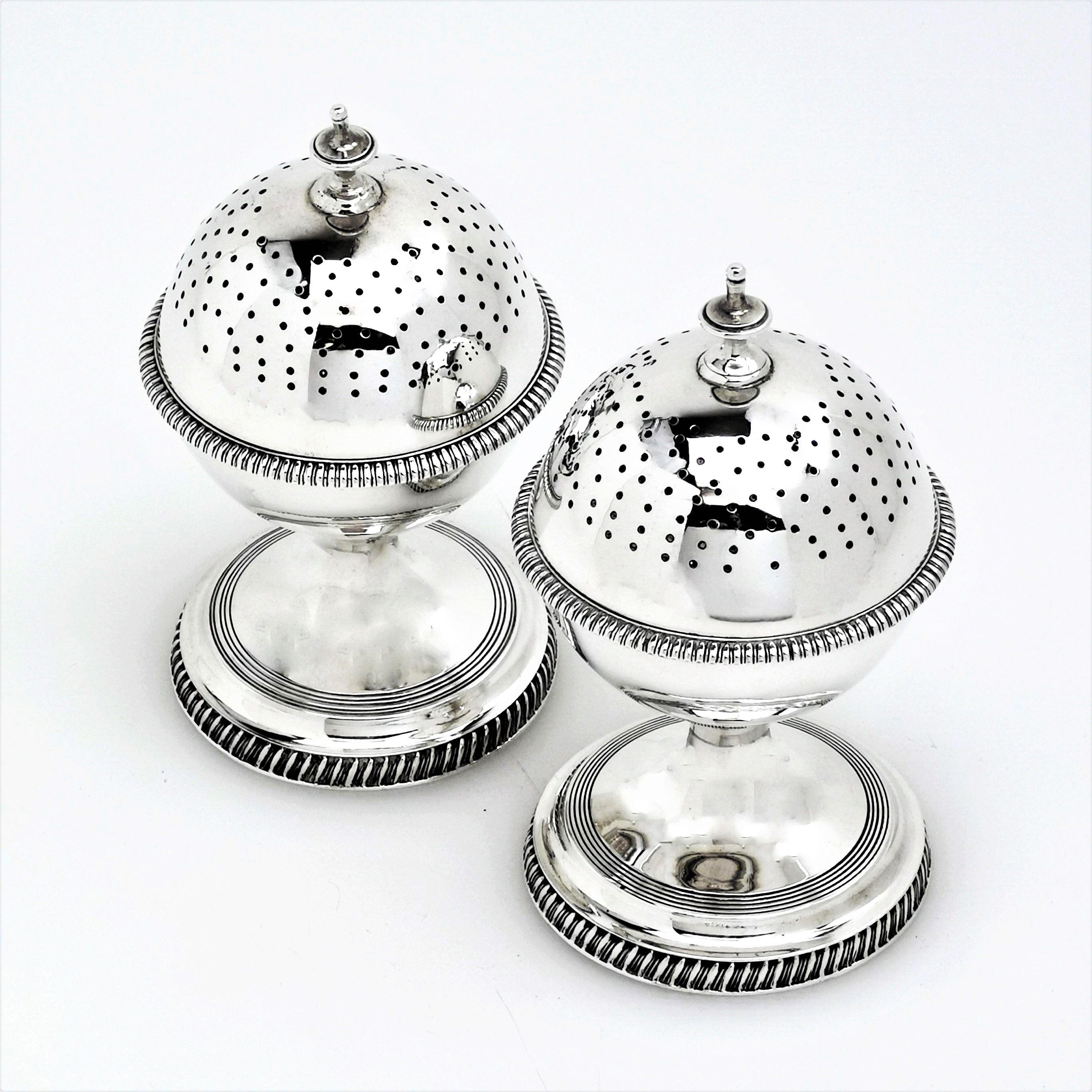 A pair of sterling Silver Georgian style globe shaped Peppers or Salt & Pepper Shakers each standing on a substantial spread pedestal foot. The Shakers each have a gadroon border around the feet and also on a girdle around the centre of the globe.