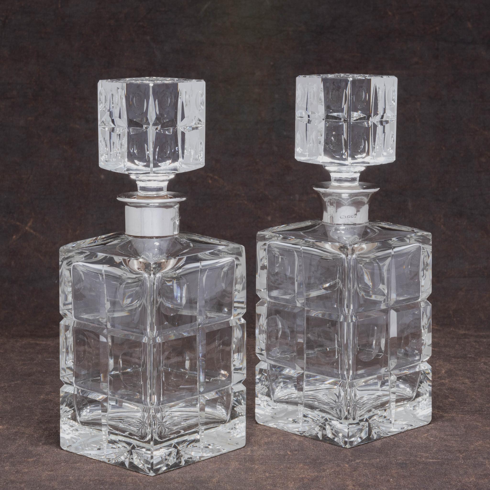 Stylishly crafted in heavy cut glass with sterling silver collars and cut glass stoppers. With a geometric circles and crosses pattern to the glass body and stopper and a star cut to the base. Both hallmarked London 1966. With maker's marks for