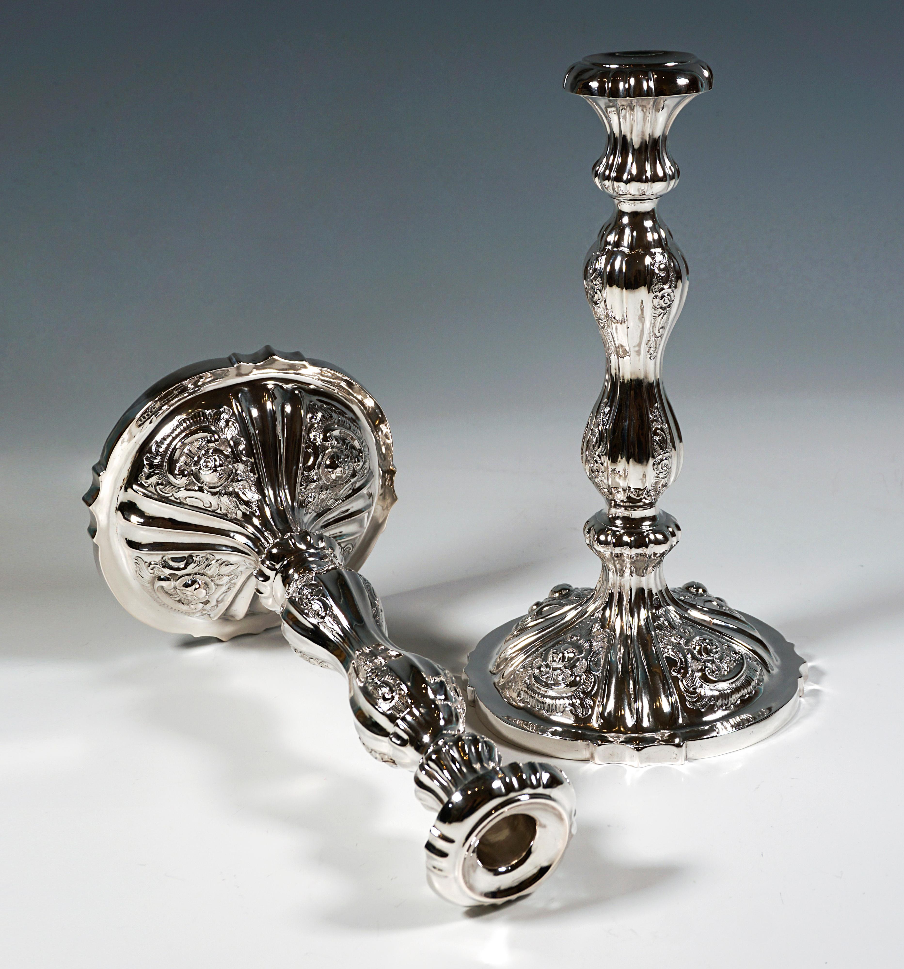 Dos candelabros festivos Biedermeier de plata sobre soporte abombado de cuatro pasos con borde curvo y puntiagudo, decoración de rosas en relieve y cincelada entre estrechos pliegues en el pie y el astil en forma de balaustre, pico en forma de