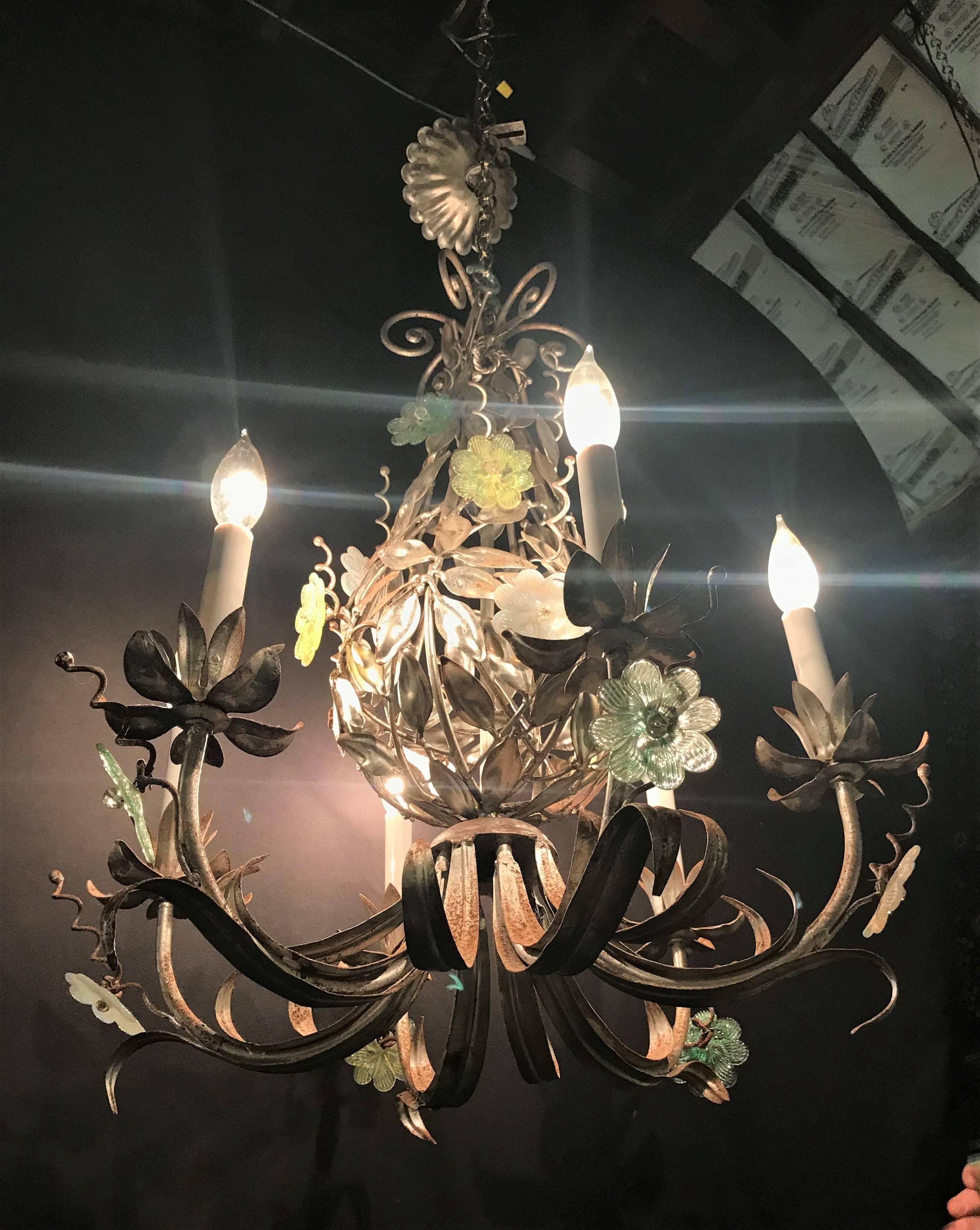 Pair of silver overlay metal chandeliers with glass Murano flowers each having six lights. This Hollywood Regency pair of chandeliers are sleek and stylish with their colored Murano floral additions. Having distressed metal frames with a matching