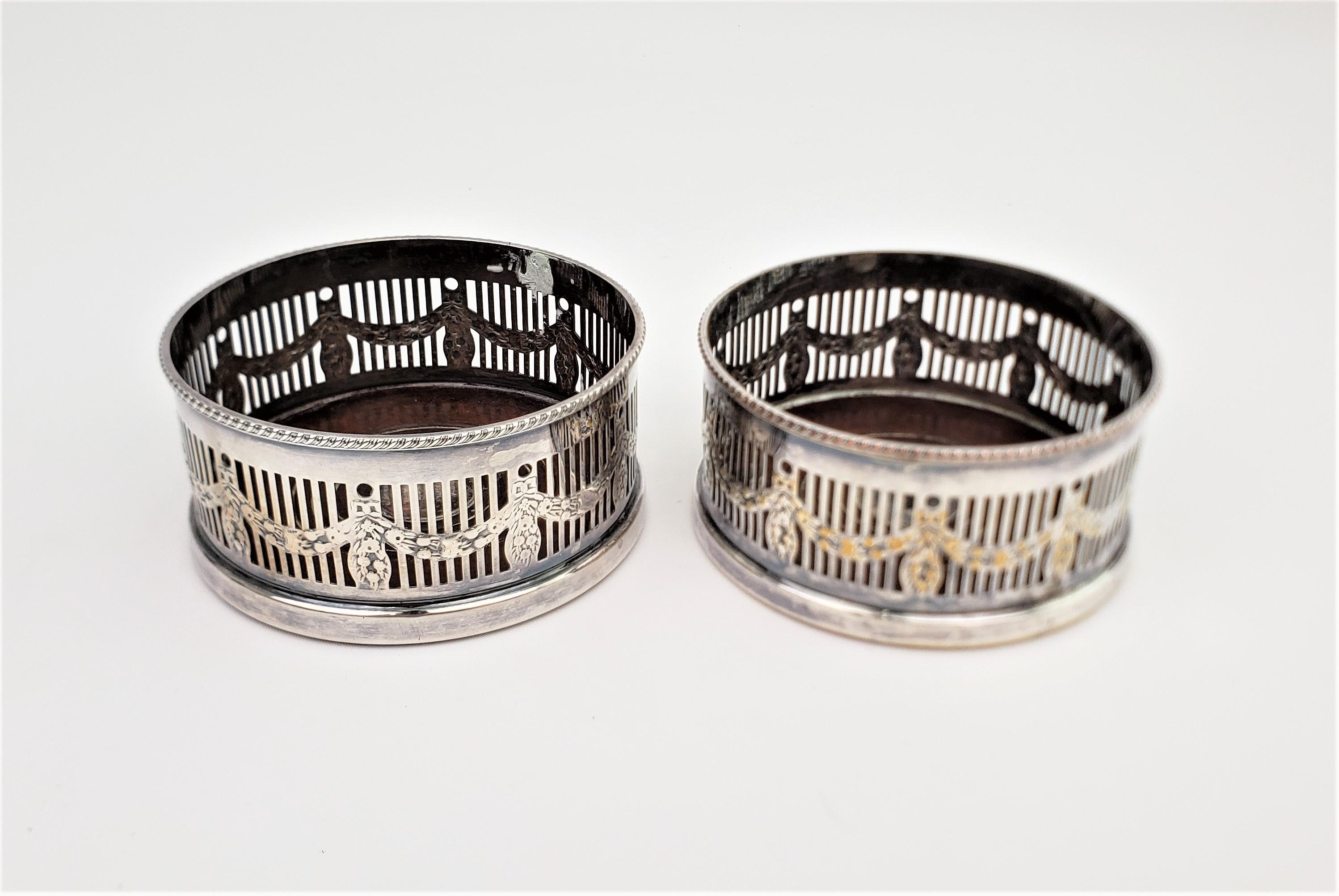 This pair of silver plated bottle coasters were made by Alpha Plate of Sheffield England in approximately 1920 in a slightly earlier Edwardian style. The bottle coasters have gallery surrounds with a garland and ribbon styled decoration and turned