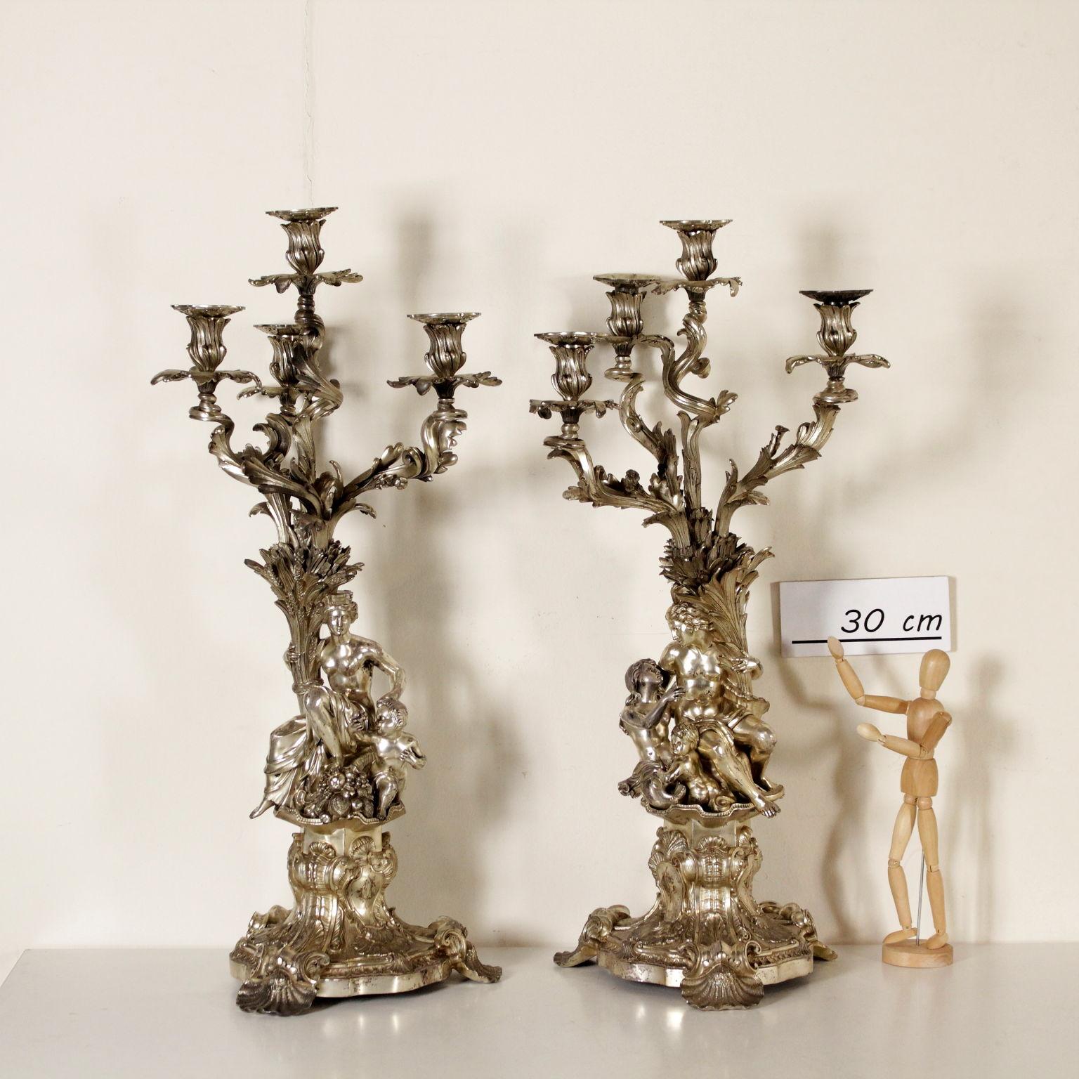 A pair of silver plated bronze candlesticks, finely chiseled. The pair of candlesticks has a Late Baroque base with three feet shaped like shells and coats of arms with the engraved initials CM. A pair of compositions on the bases: on the first one,