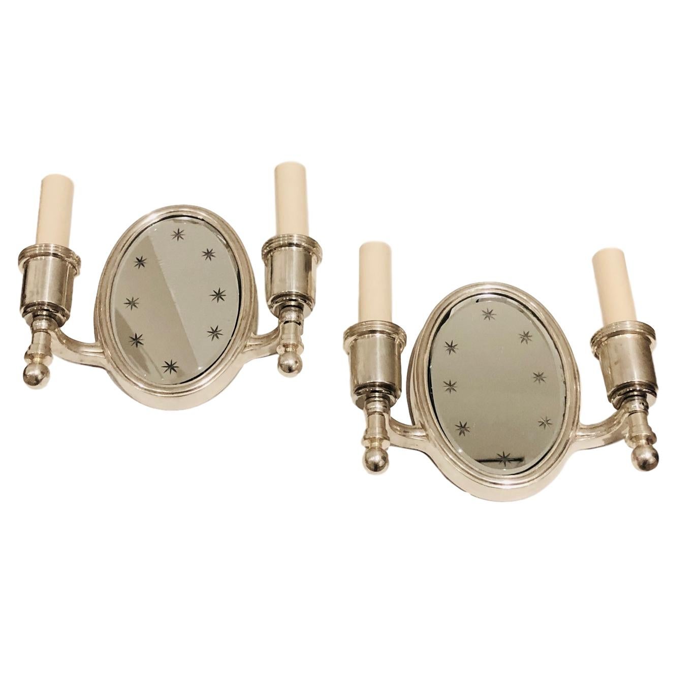 Coppia di appliques inglesi a due bracci, degli anni '30 circa, placcate in argento e con retro specchio inciso con motivo a stella.

Misure:
Altezza 7,5
Larghezza 8,5
Profondità 2,5