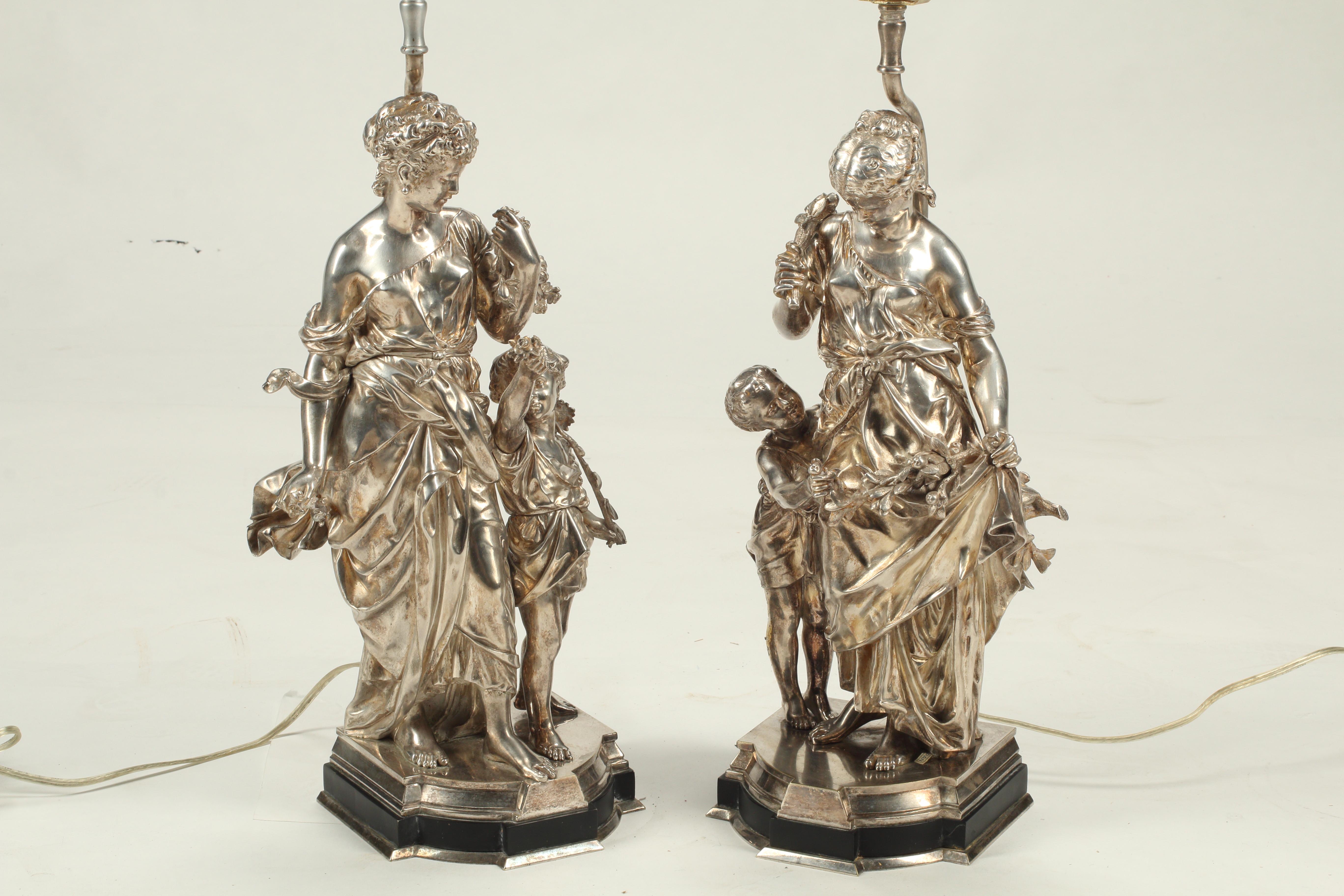 A pair lovely of 19th century silvered bronze figural lamps each featuring a female figure dressed in flowing robes holding florals with cherubs or puttis by their sides. The hand caste bronze exhibits remarkable detail from the texture of each