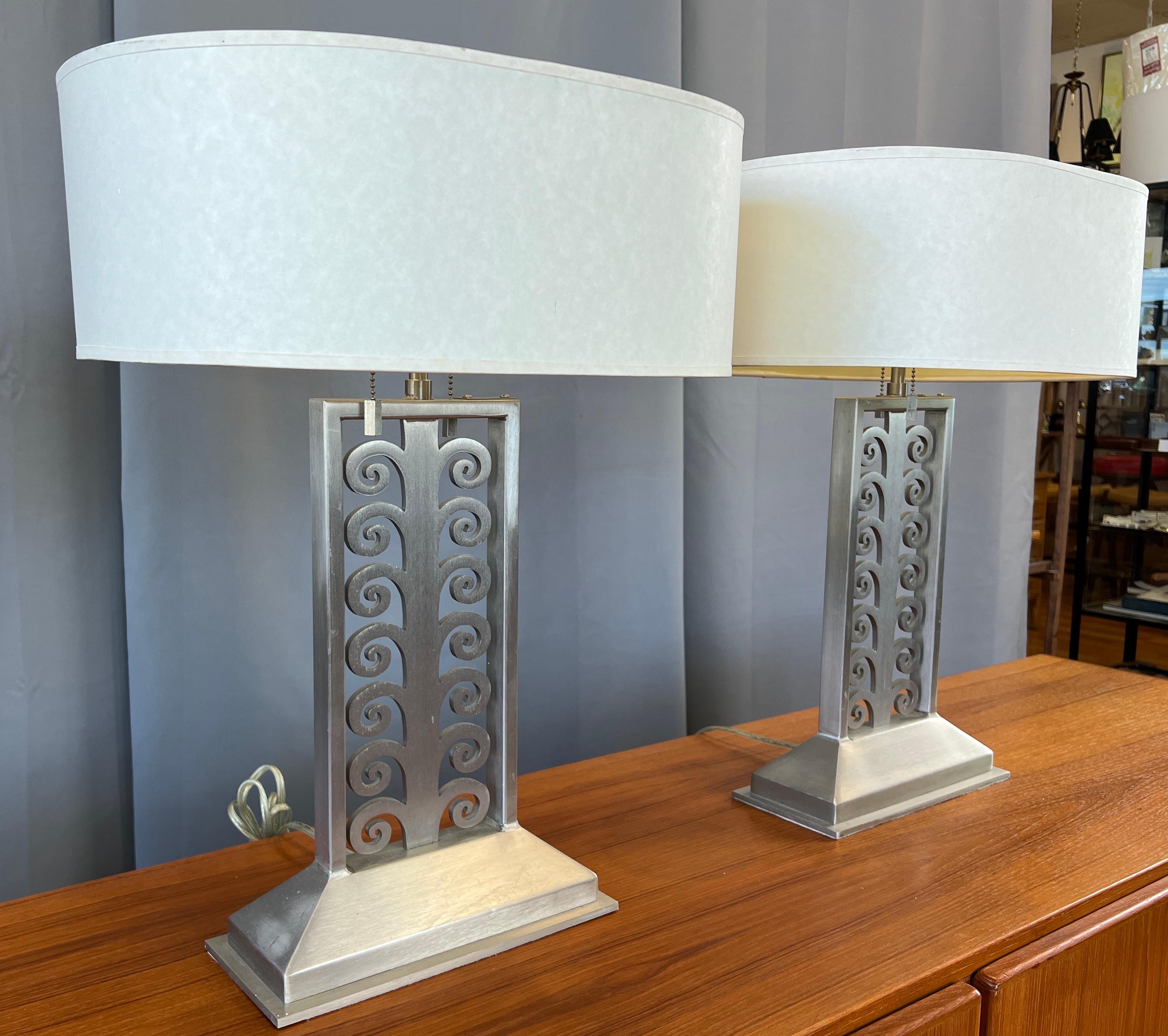 Offered here are a pair of Sirmos designed and made table lamps. Both have labels on their underside. 
In brushed stainless steel, with the center a framed laser cut scroll work design, on substantial bases.
Cream color oval shape lamp shades top