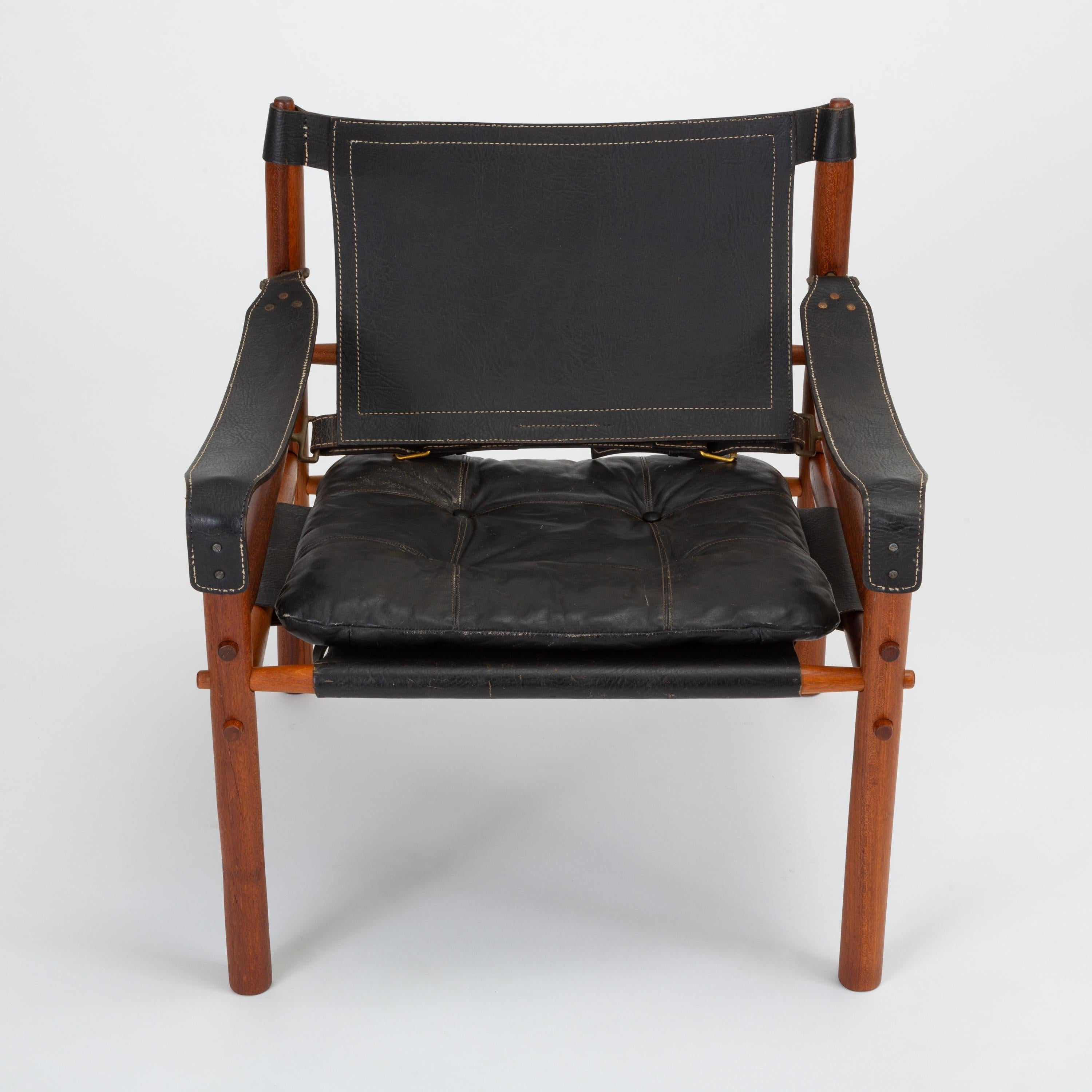 A pair of 'Sirocco' safari chair designed by Arne Norell for his eponymous company, Norell Möbel AB of Småland, Sweden. This pair features a solid teak frame strapped together by leather slings with brass fittings and black leather with contrast