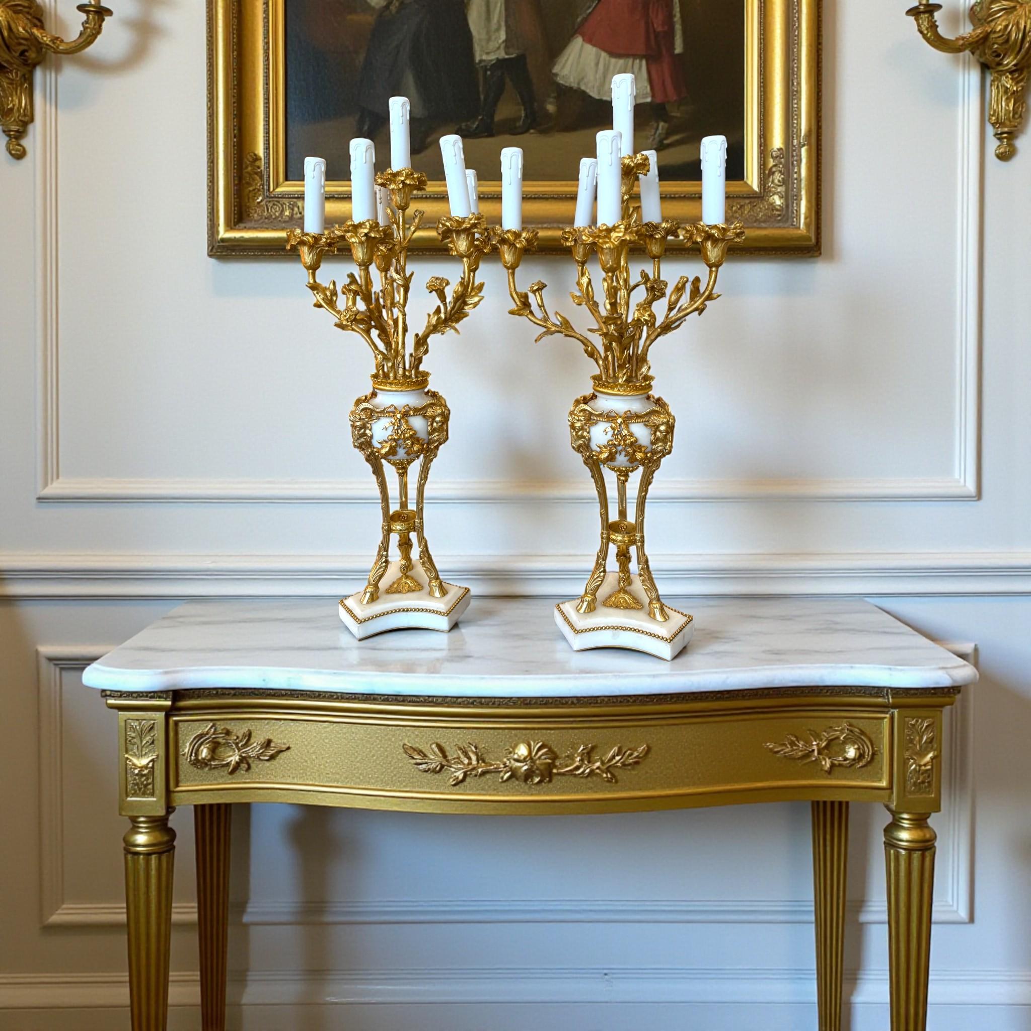 Una squisita coppia di candelabri finemente lavorati in bronzo dorato e marmo bianco di Carrara, risalenti al XIX secolo.

Ogni candelabro poggia su una base di marmo bianco, arricchita da un fregio di perline in bronzo dorato, da cui si erge un