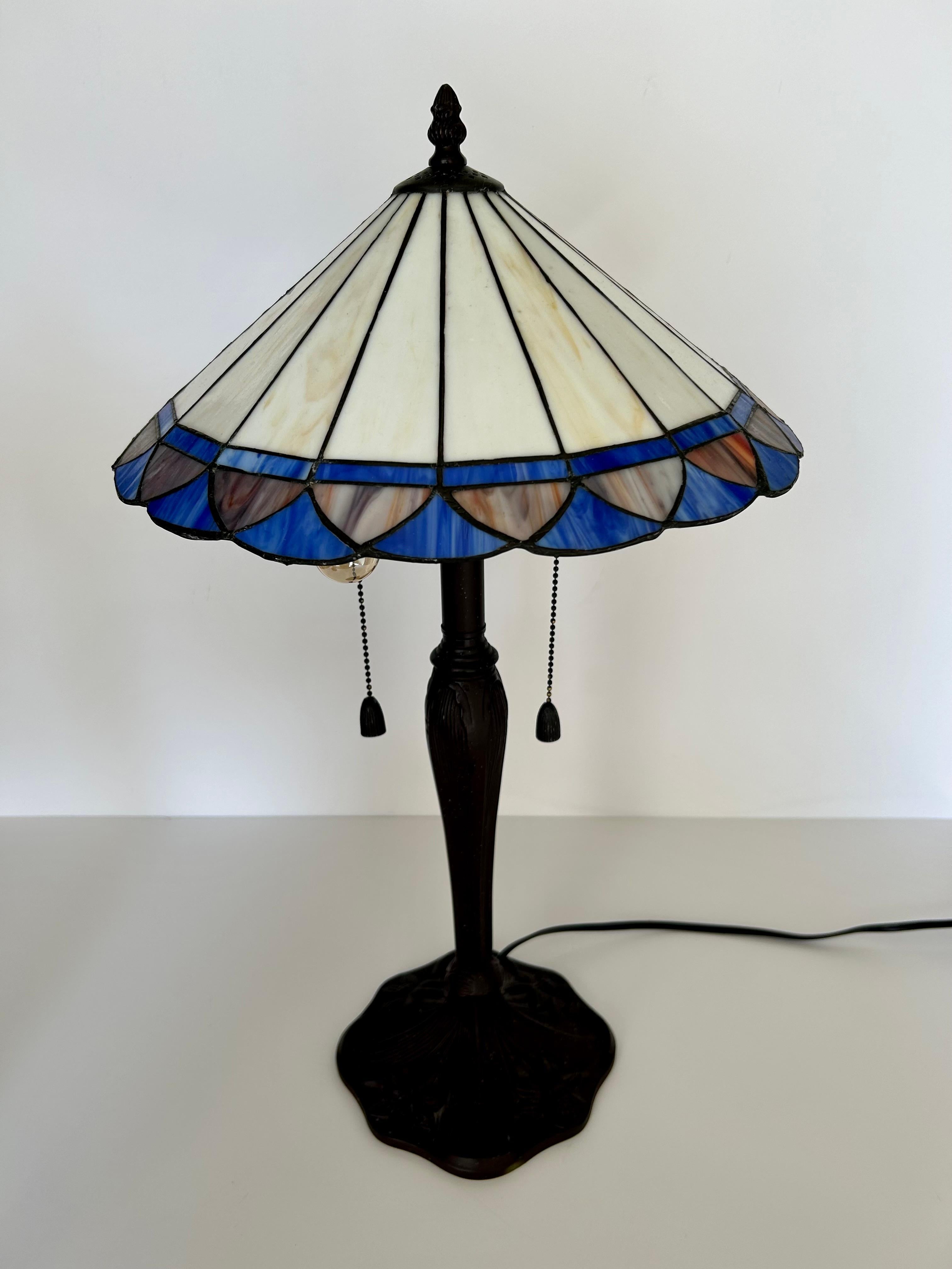 This is a wonderful pair of twentieth century, American slag glass lamps. Wonderful conical shades in tones of cream with brilliant indigo glass on the scalloped border. Cast metal bases in sinuous Art Nouveau design. Original cast metal