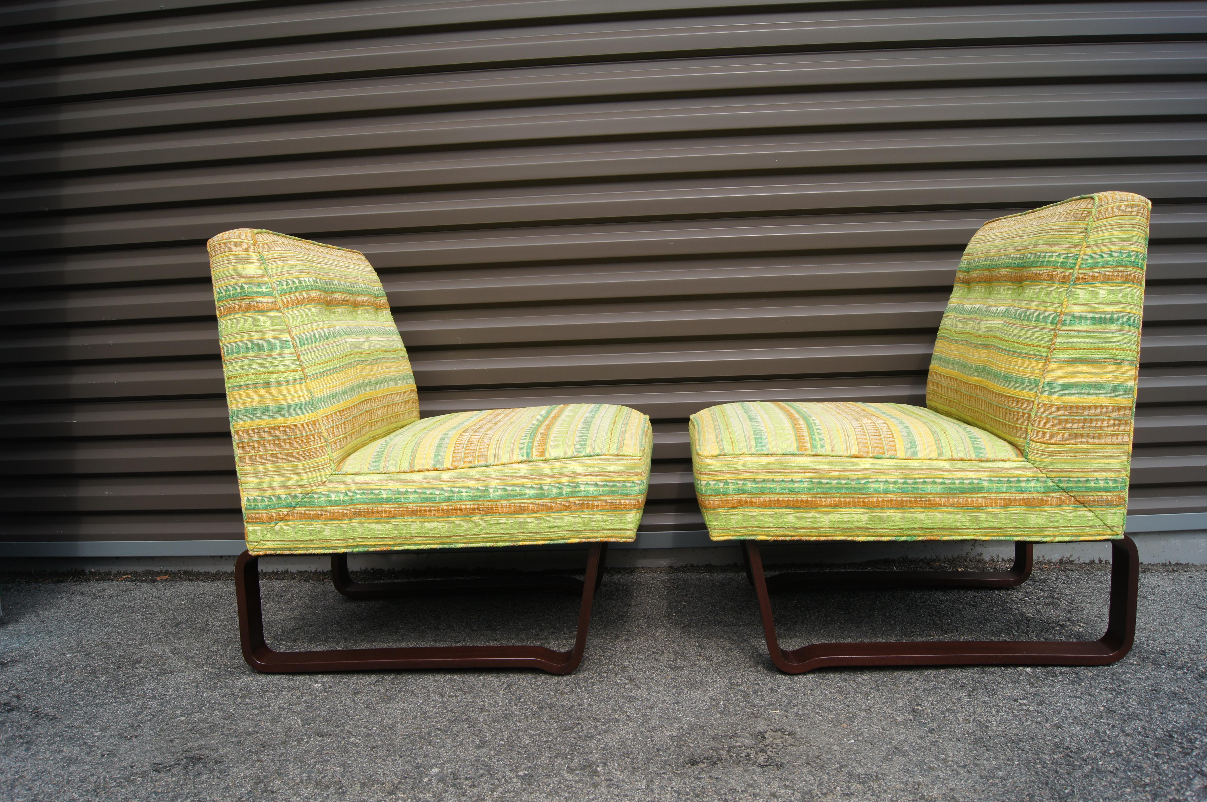 These slipper chairs were designed by Edward Wormley and produced by Dunbar in 1949. The sled-style mahogany legs support a comfortable wide seat with an inclined back. The pair are upholstered in their original textile, a weave of greens, oranges,