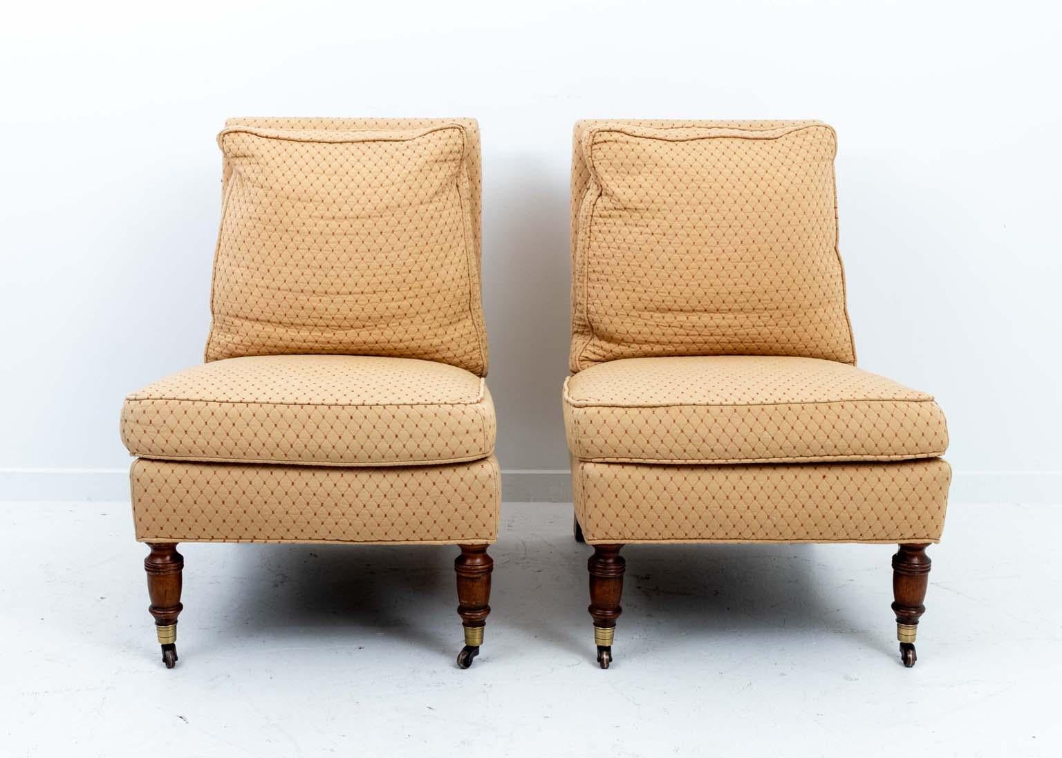 Comfortable pair of upholstered armless chairs with turned mahogany front legs in brass casters. The back legs are mahogany and straight. The back pillow is feather down filled and is attached. 
