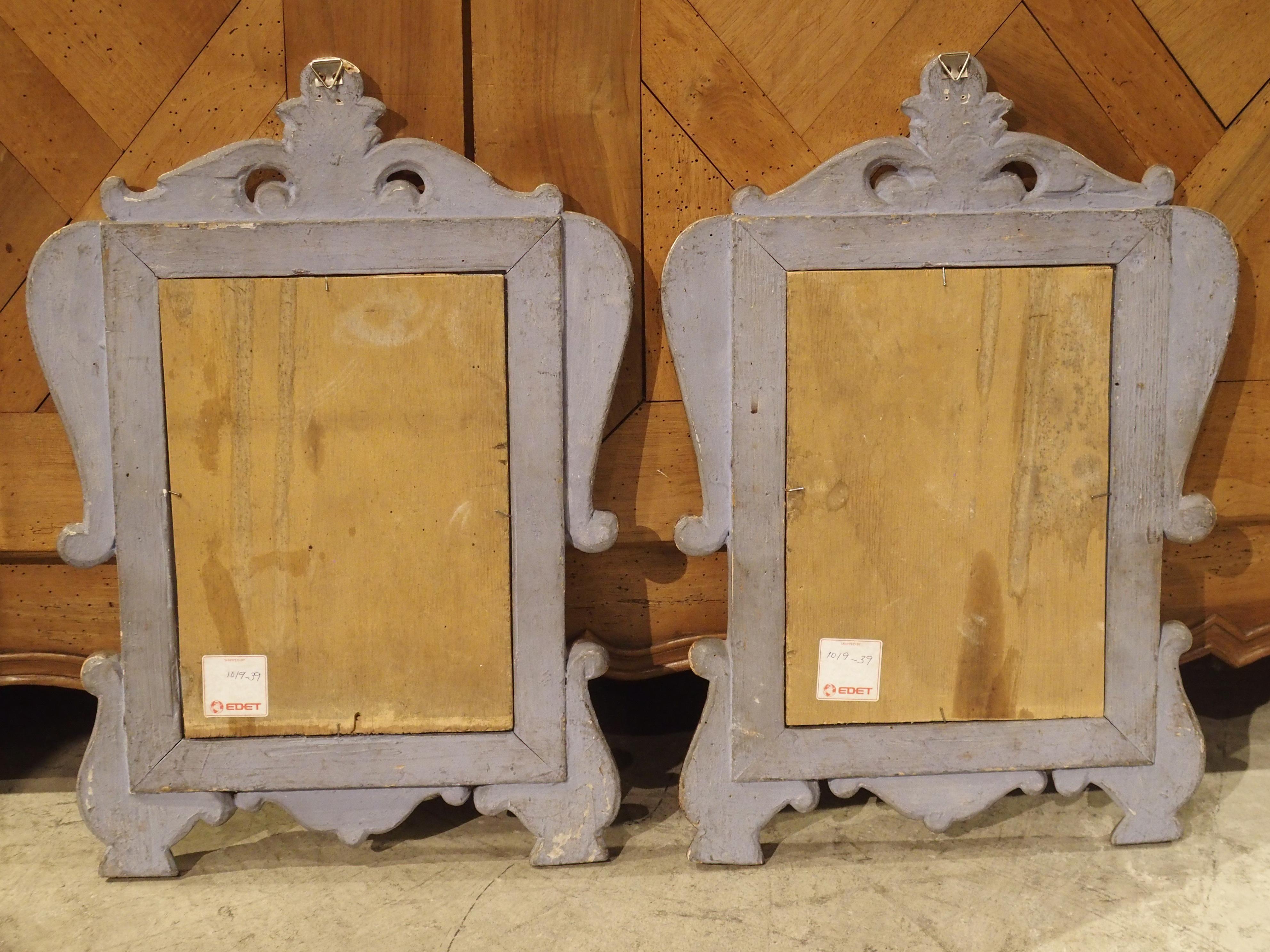 These small and decorative wall mirrors are from Italy and date to the late 1700s. They have a simple rectilinear form adorned with carved scrolling motifs on the crown, at the shoulders, and flanking the lower corners. A small, stylized