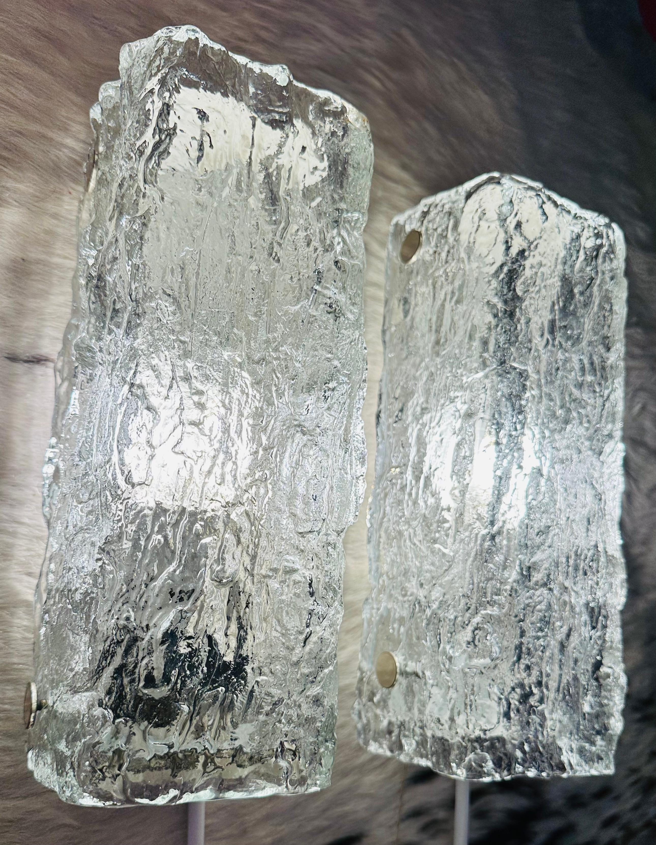 Zwei kleine Wandleuchten aus Eisglas aus den 1970er Jahren, hergestellt von dem gehobenen deutschen Leuchtenhersteller Kaiser Leuchten. Das rechteckige, dicke, strukturierte Glas wird auf einen weiß lackierten Metallrahmen geschraubt, der einfach in