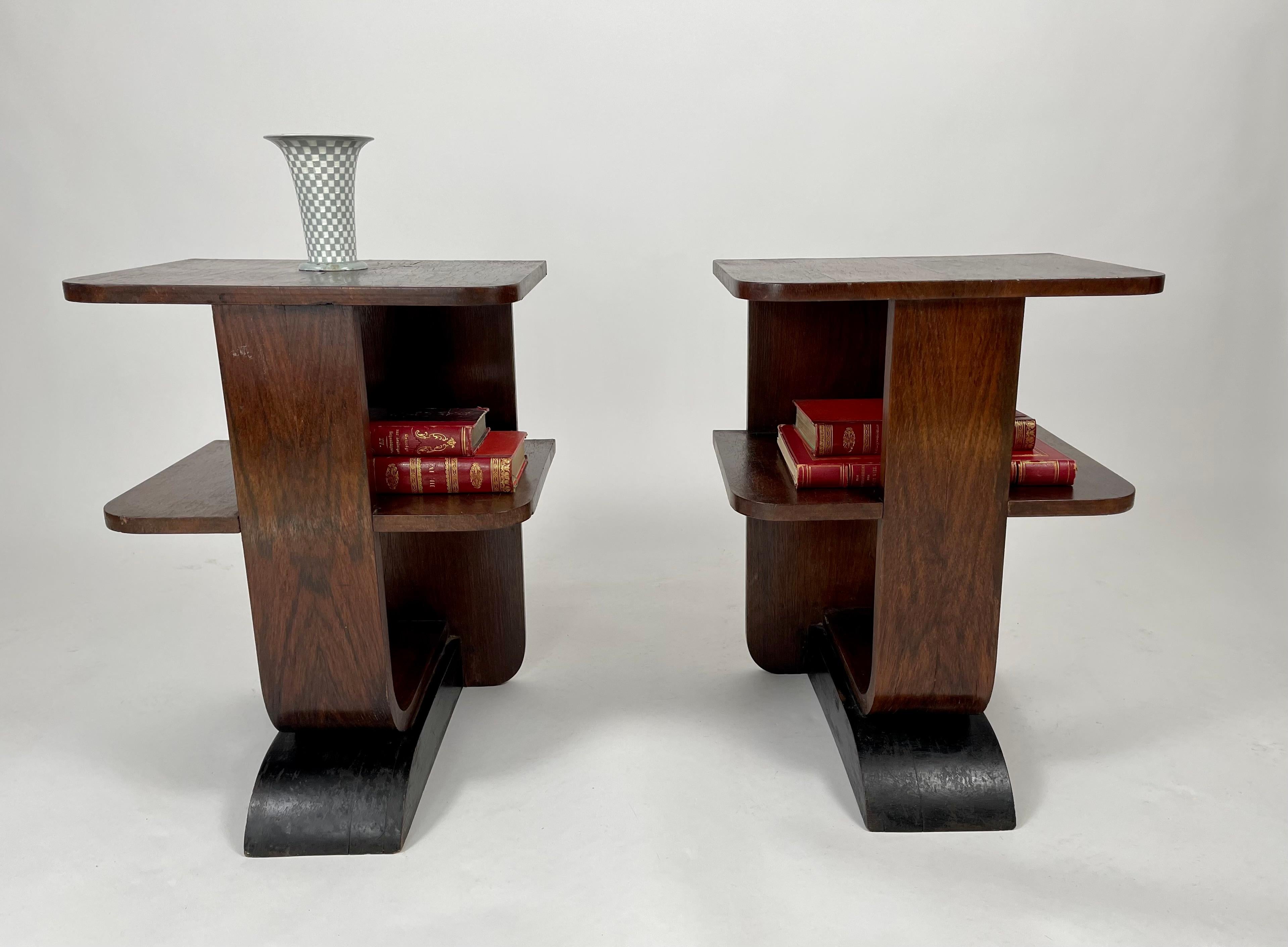 A pair of small scale Art Deco period end tables or night stands, the tops with book matched walnut veneers over a central shelf, with an ebonized curved base, With their sculptural form and good lines, these tables would be good individually next