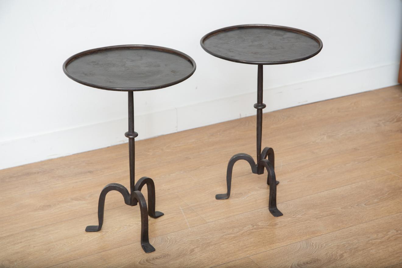 Pair of small black iron side or drinks tables, in stock. This stunning wrought iron tripod side table is an eye-catching addition to any home decor. Its round top features a lip, and its hammered metal frame has a beautiful black patina that gives
