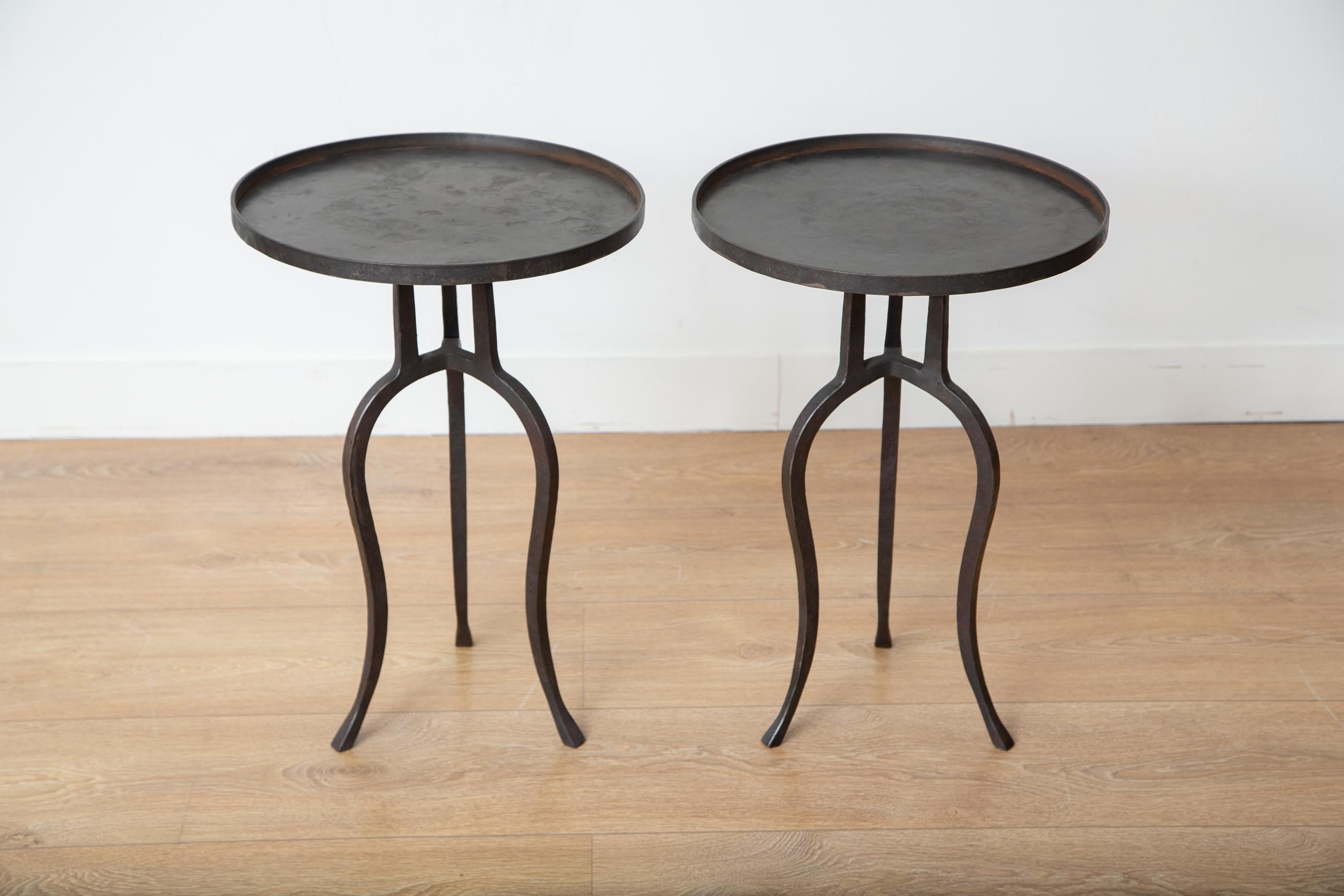 Pair of small black iron side tables, in stock.
This stunning wrought iron tripod side table is an eye-catching addition to any home decor. Its round top features a lip, and its hammered metal frame has a beautiful black patina that gives it a