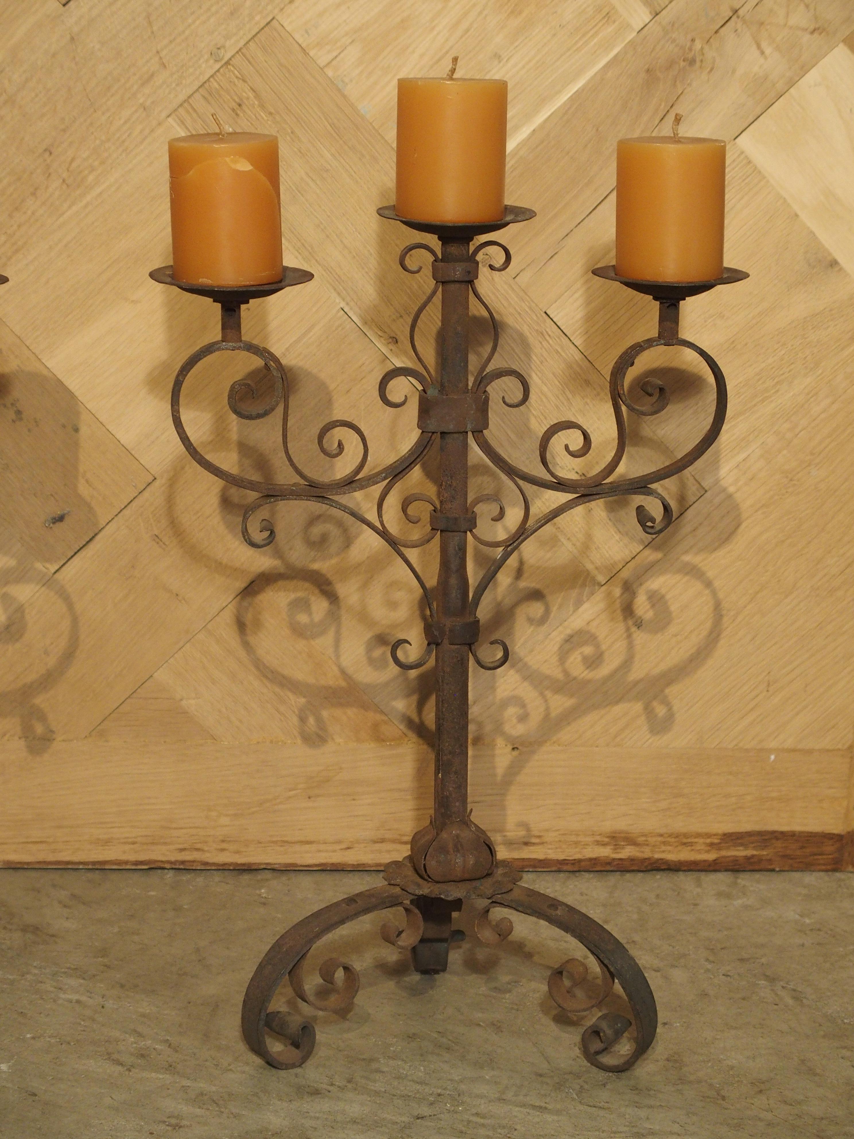 From Italy, this pair of wrought iron candelabras have three arms with the center arm being the highest. The candelabras are filled with C and S scrolls cascading out from a central iron stem. The bottom is made up of three inward scrolled feet. All