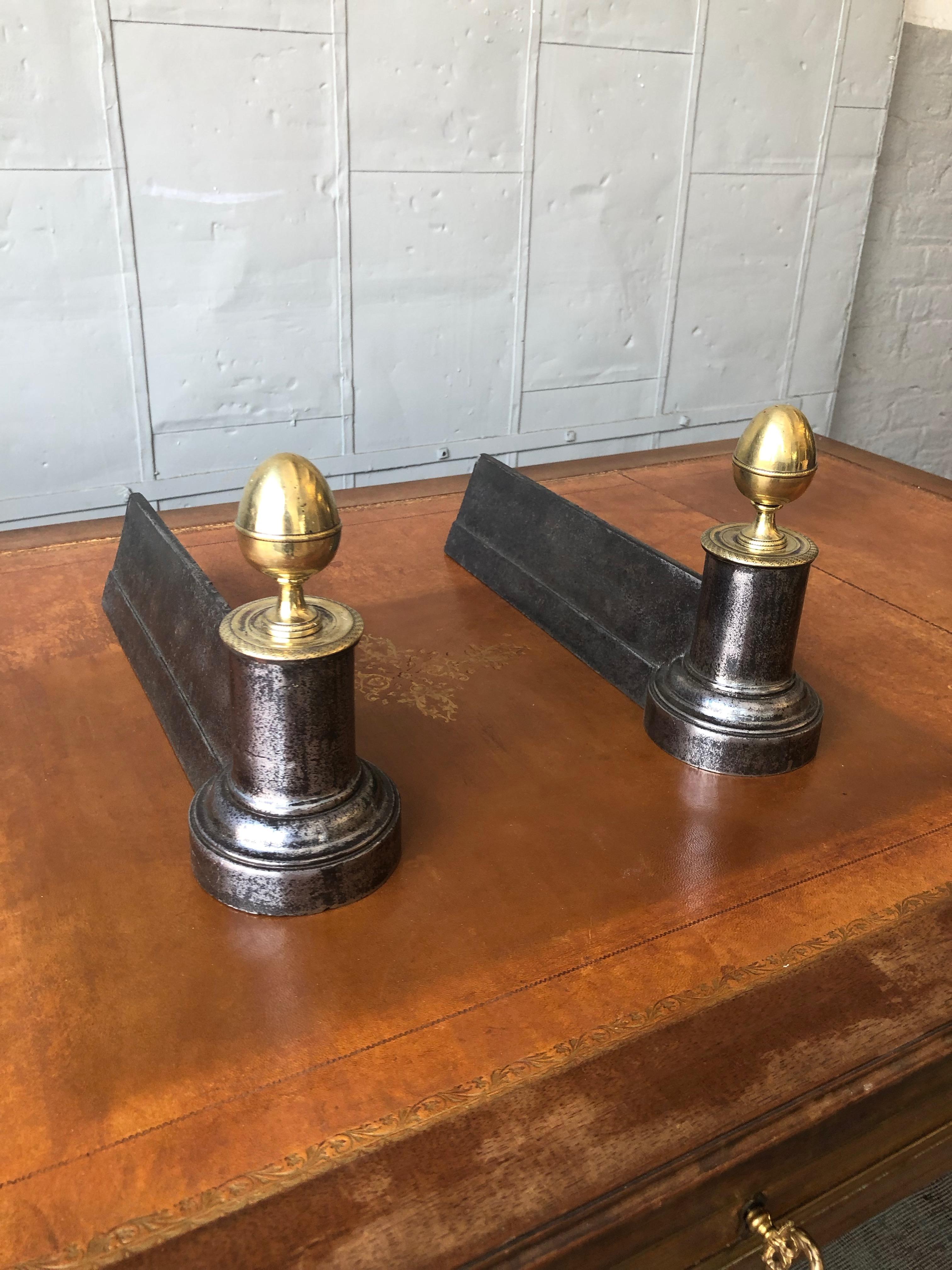 A pair of 19th century French fire andirons in the Empire style. The polished iron supports are complimented with oversized brass finials resting on classical columns. The andirons have recently been polished, and they are in very good