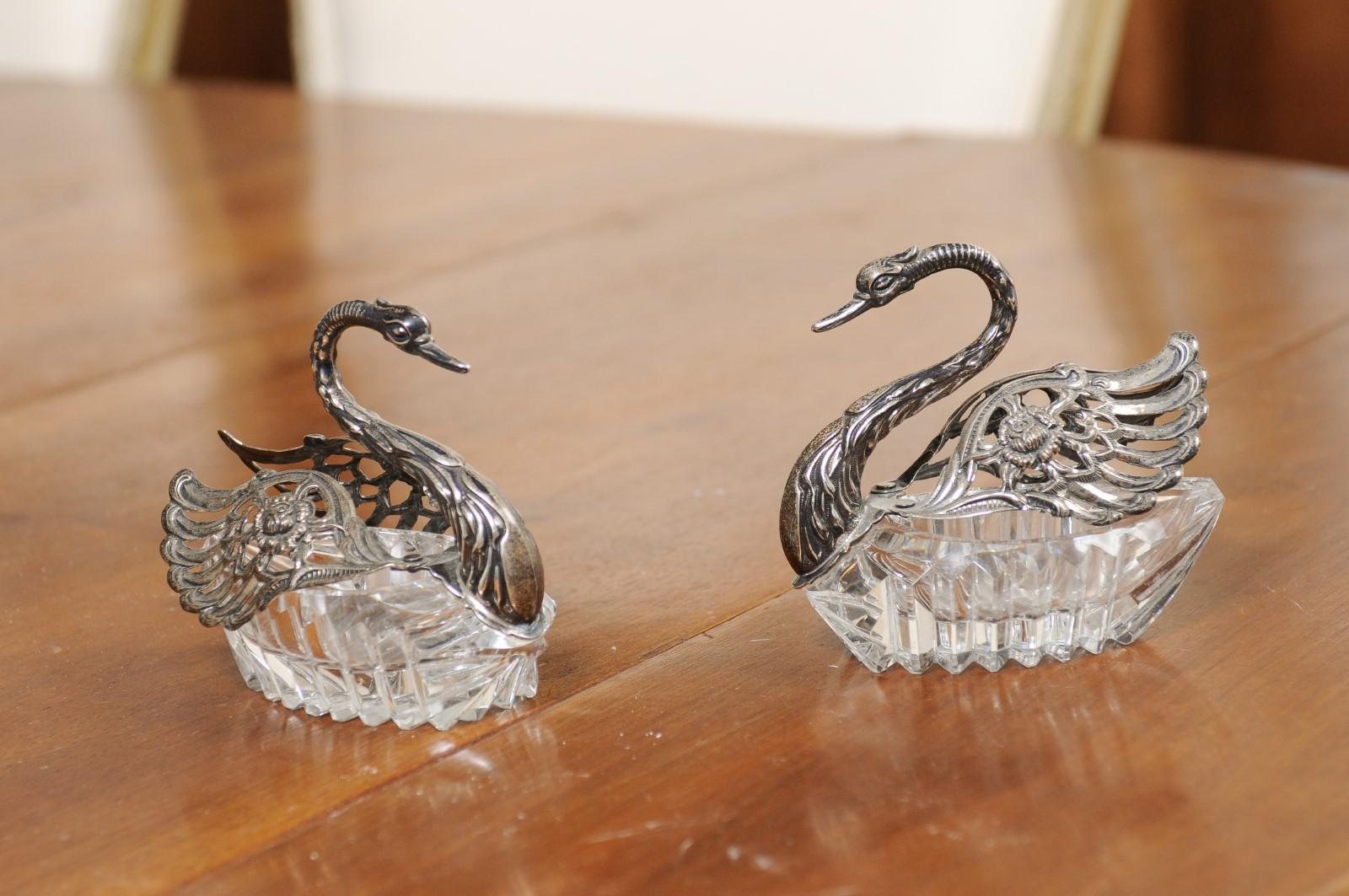 A pair of English crystal swans from the 20th century, with silver wings that open. Created in England during the 20th century, each of this pair of crystal swans attracts us with its nicely detailed body and contrasting colors. The lower part of