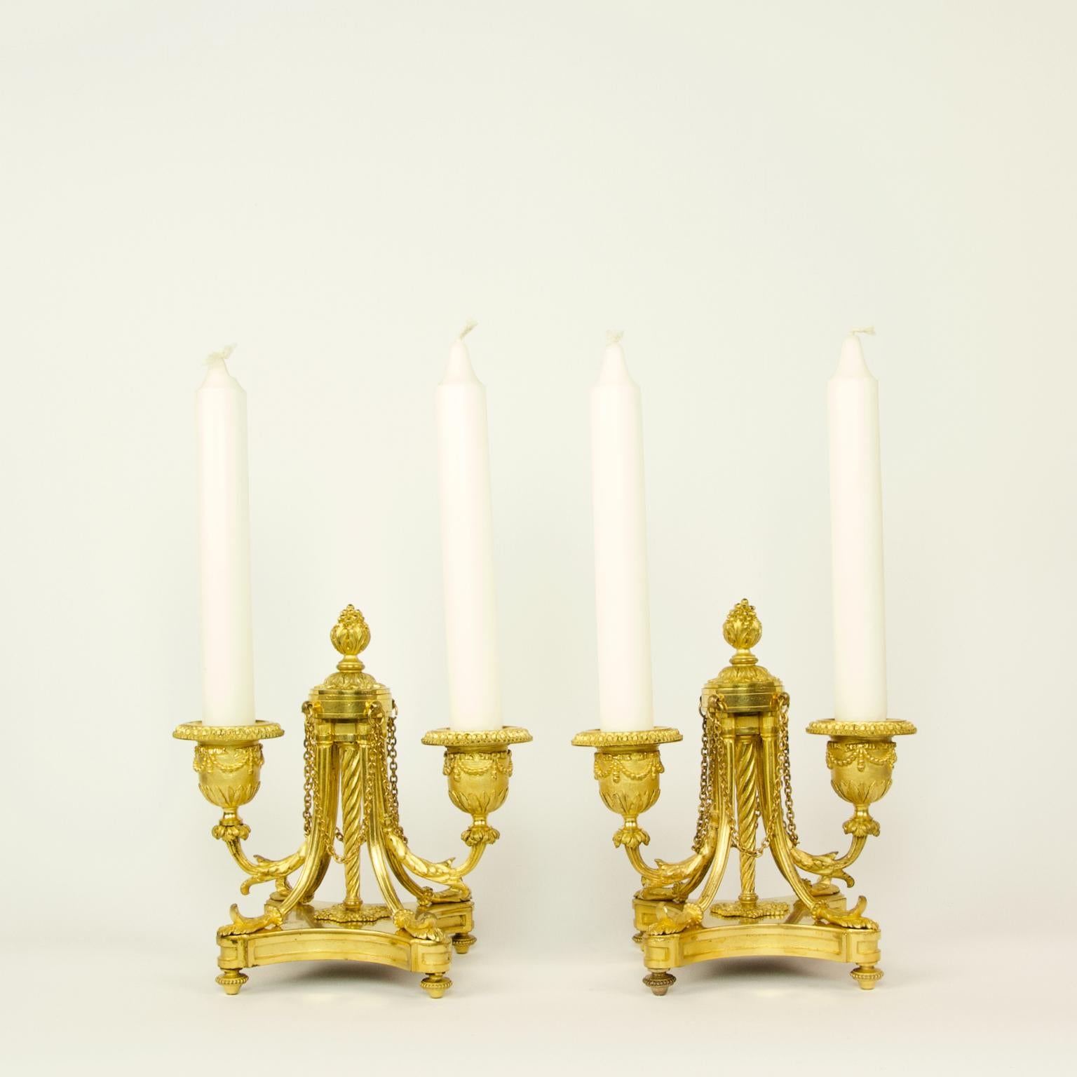 Pair of small French 19th century/Napoleon III Louis XVI style gilt bronze two-light candelabra

Each candelabra featuring two fluted light arms with foliage decoration and bell-shaped nozzles or bobeches. The light arms are supported by a