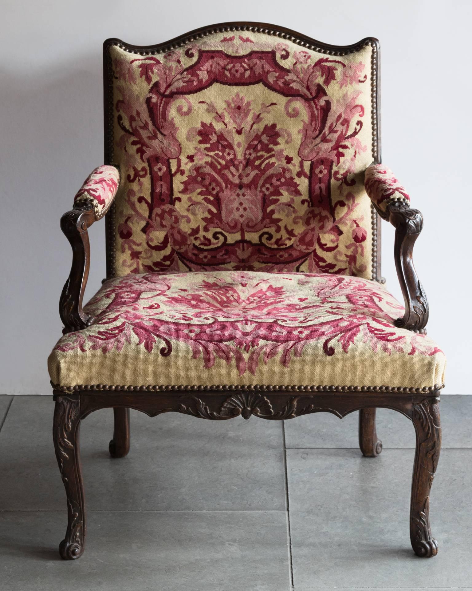 A pair of Louis XV armchairs of small proportions carved in beech with scrolling acanthus leaves, shells and lambrequins. Evidence of old paintwork on the underneath of the timber. Upholstered in later petit point needlework in sand and dark fuchsia