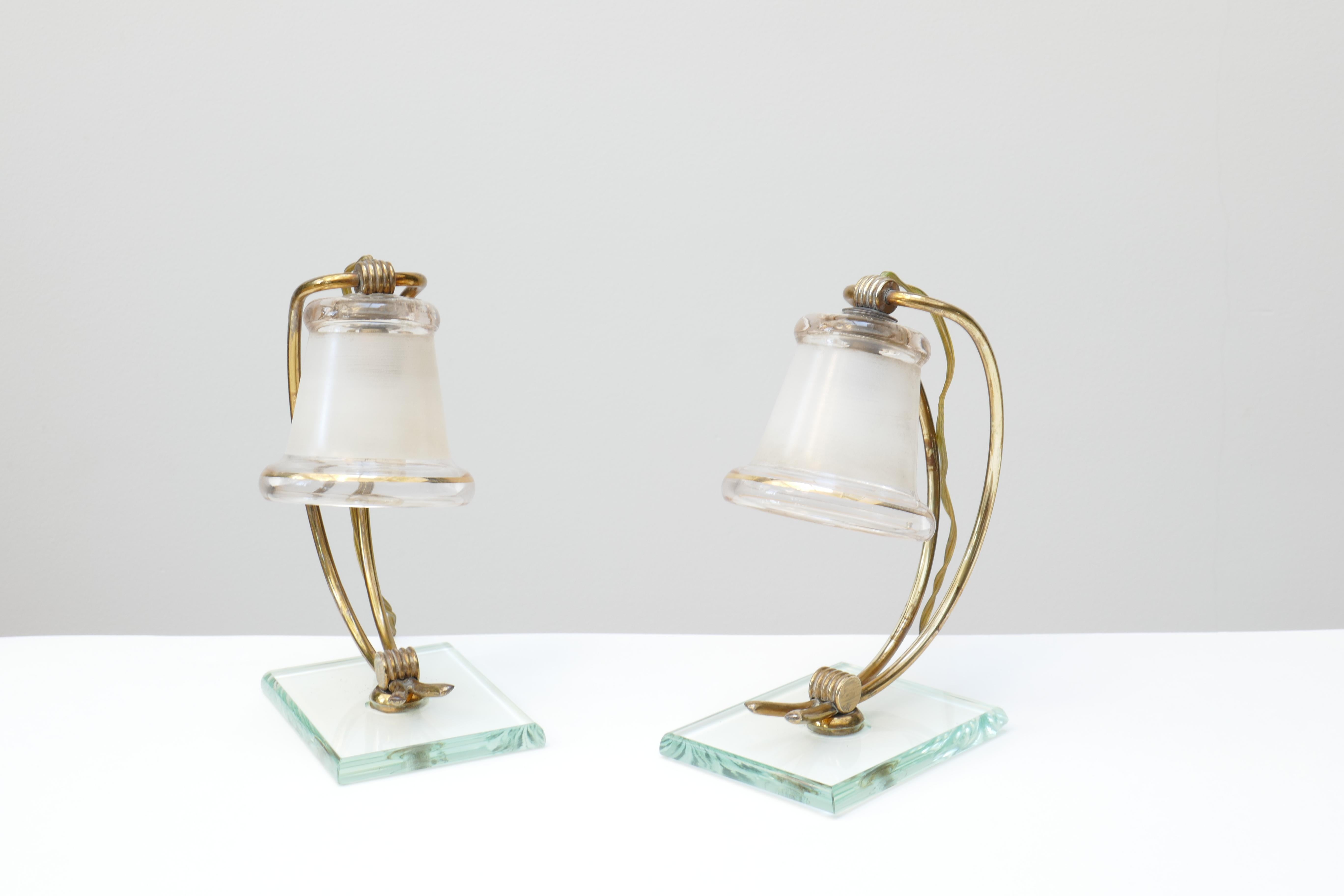 Une paire unique de petites lampes de table vintage italien dans le style de Fontana Arte . Une tige en laiton à double courbure tient un verre en forme de cloche avec des bords dorés. L'abat-jour en verre a des bords transparents tandis que la