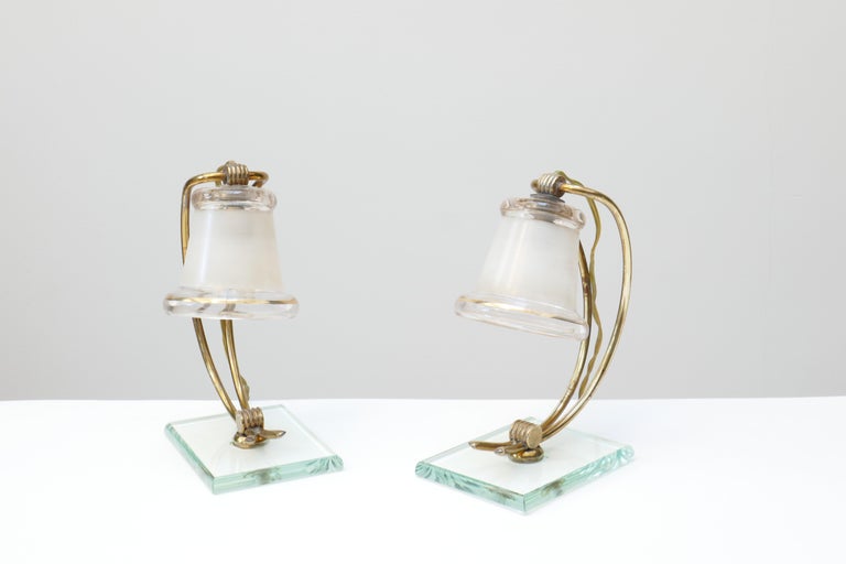A unique pair of small table lamps vintage Italian in style of Fontana Arte . A double curved brass stem hold a bell shaped glass with gold rims . The glass shade has transparent rims whilst the central part is opal glass to diffuse the light . The