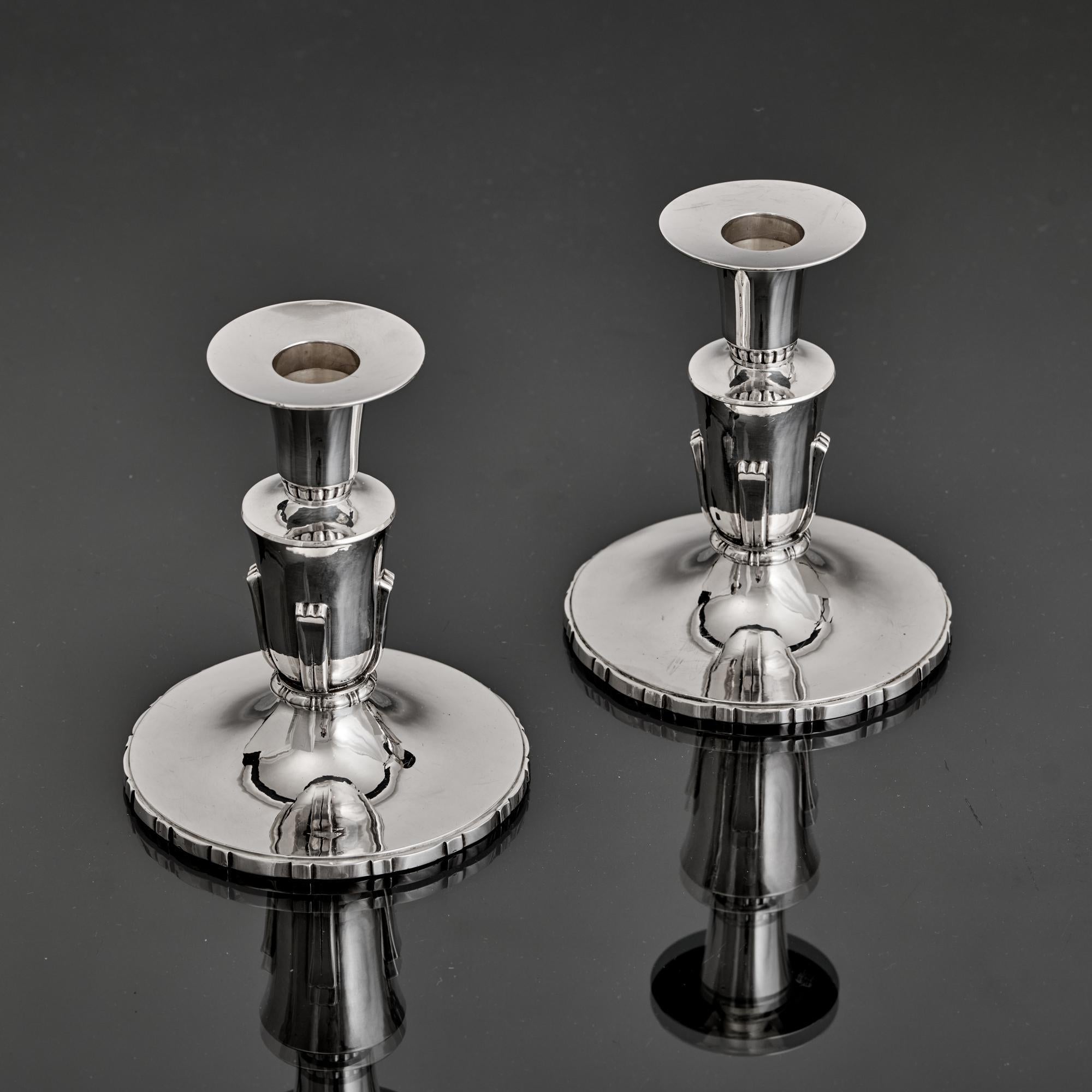 Pareja de pequeños candelabros de plata maciza labrada a mano, con rasgos de diseño clásicos del estilo Art Déco y fabricados por Robert Edgar Stone, orfebre y diseñador que produjo una orfebrería distintiva y de gran calidad.

Los candelabros son