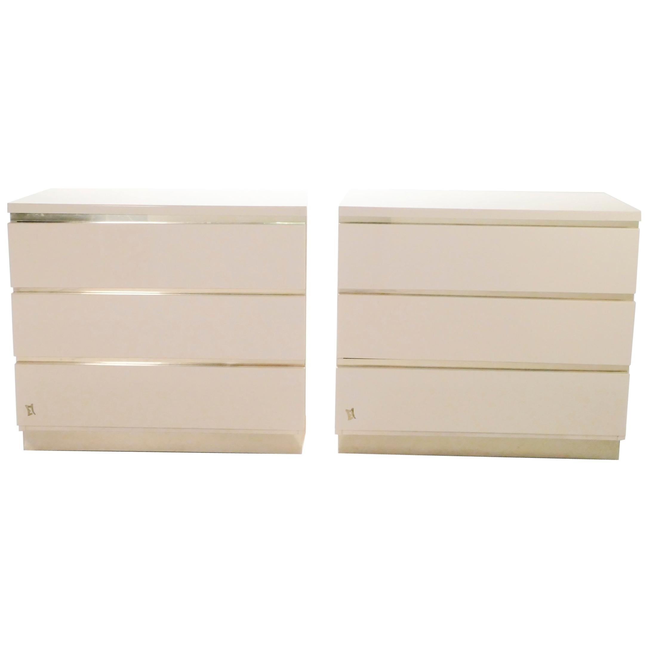 Crisp white lacquer, paired with bright brass accents, feels creamy and luxe on this pair of chests of drawers. Their boxy, simple style is typical of both the 1970s and designer Jean Claude Mahey for Maison Romeo. Whether used as two small,