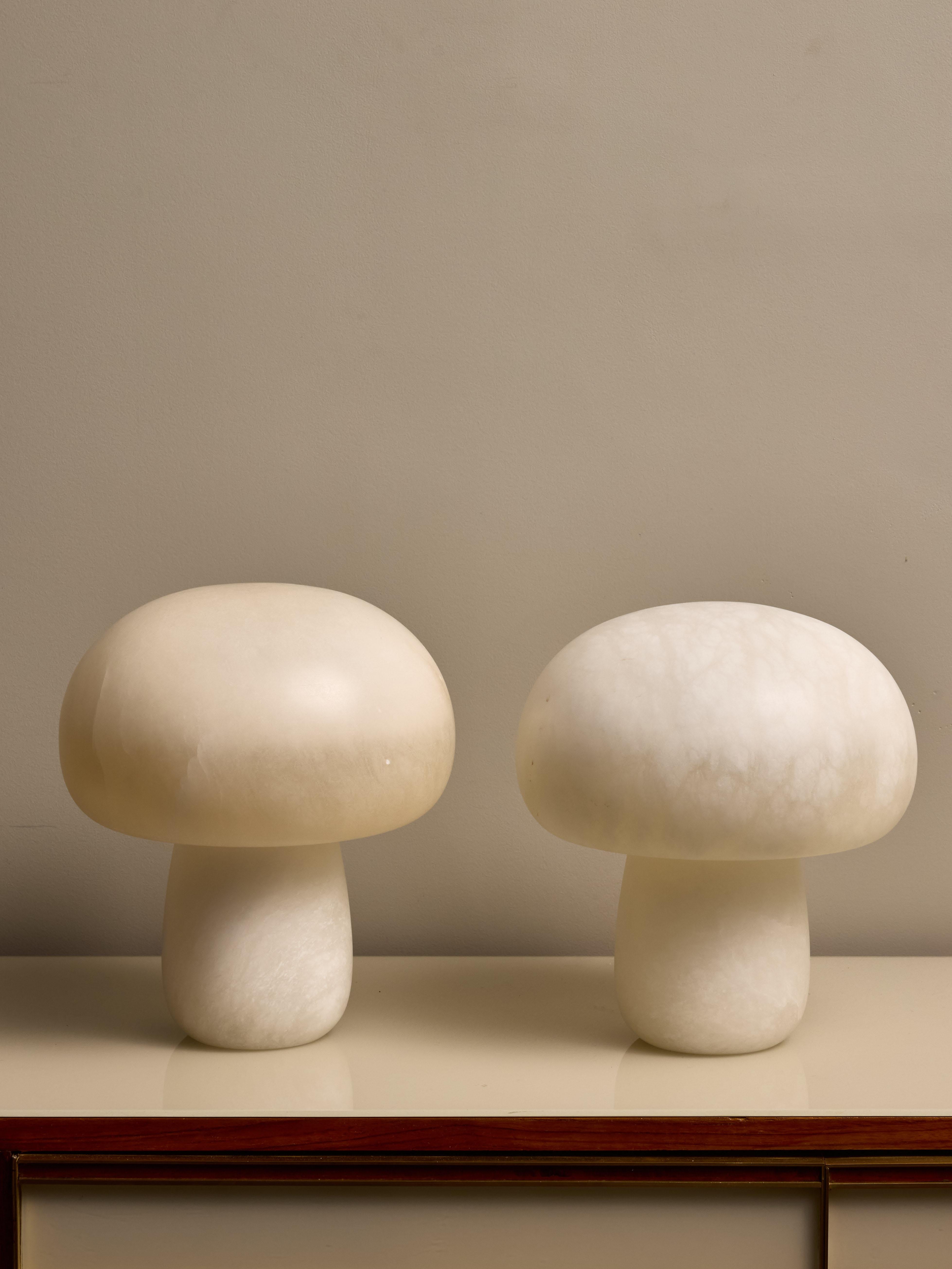 Paire de lampes de table en albâtre dont la base supporte une seule source lumineuse, surmontée d'un autre élément doucement incurvé. Le design général rappelle la forme d'un champignon.