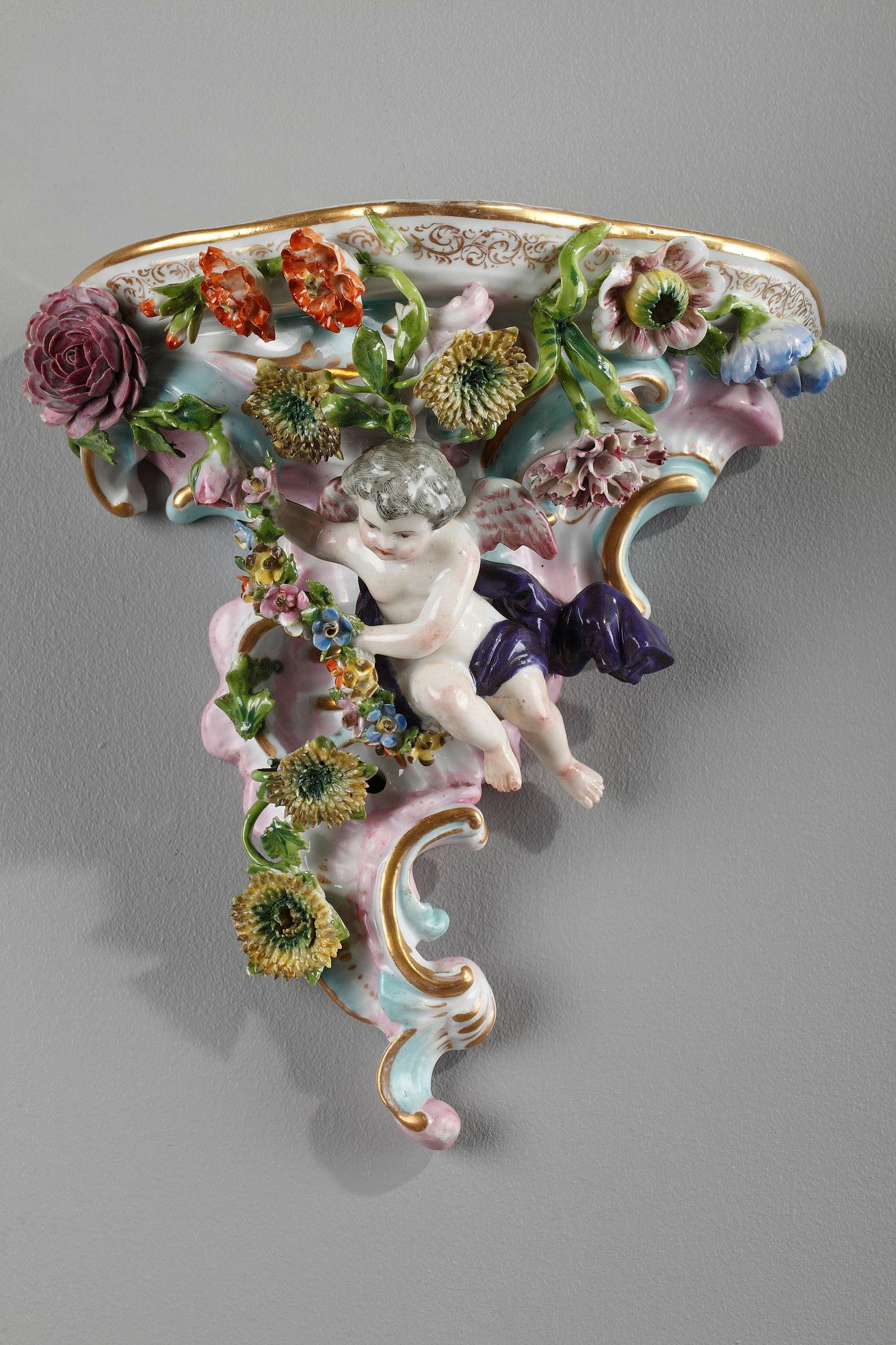Two rocaille brackets in enamelled porcelain in the style of Meissen manufacture. They are decorated with winged putti draped in purple and individualized flowers. This very fine work makes it possible to differentiate the various species of