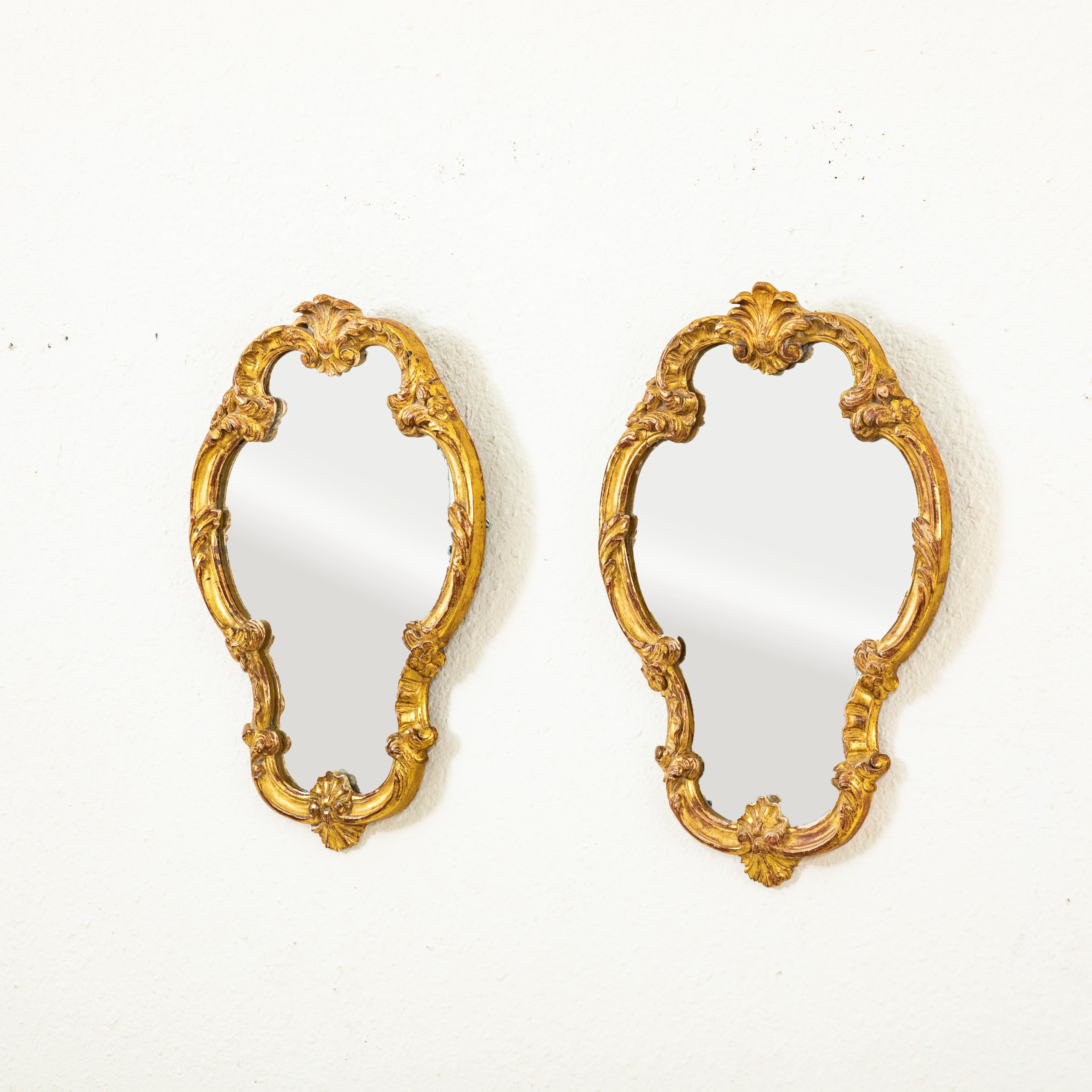 Questa coppia di specchi in legno dorato in stile Reggenza francese di piccole dimensioni, risalenti all'inizio del XX secolo, presenta il vetro al mercurio originale. Ogni specchio è decorato con un motivo a conchiglia nella parte superiore e