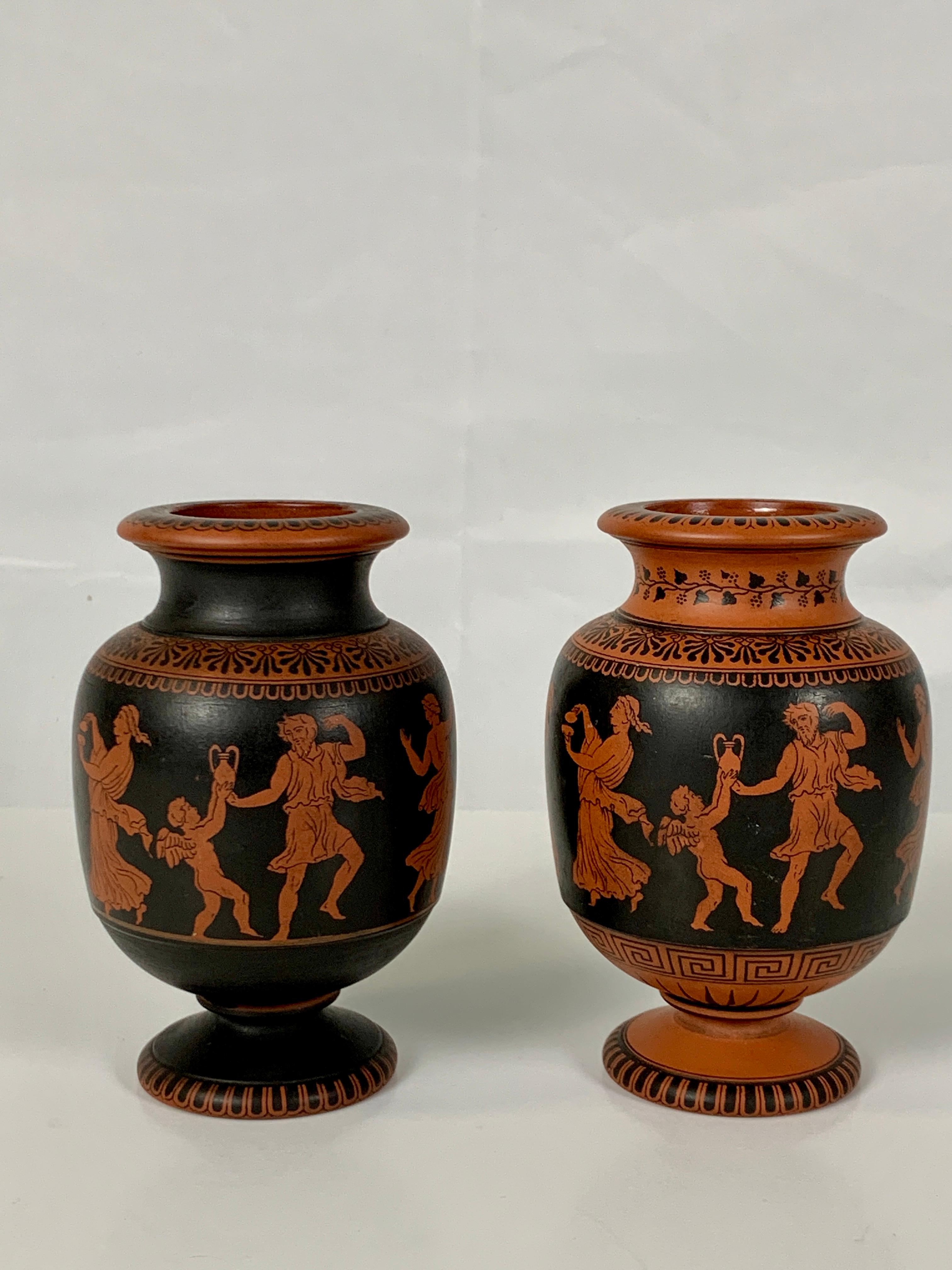 A lovely pair of small terracotta vases showing a celebration with classical figures in orange silhouette dancing and playing instruments on a black ground. The neoclassical decoration is continued on the shoulders, each of which has a band of