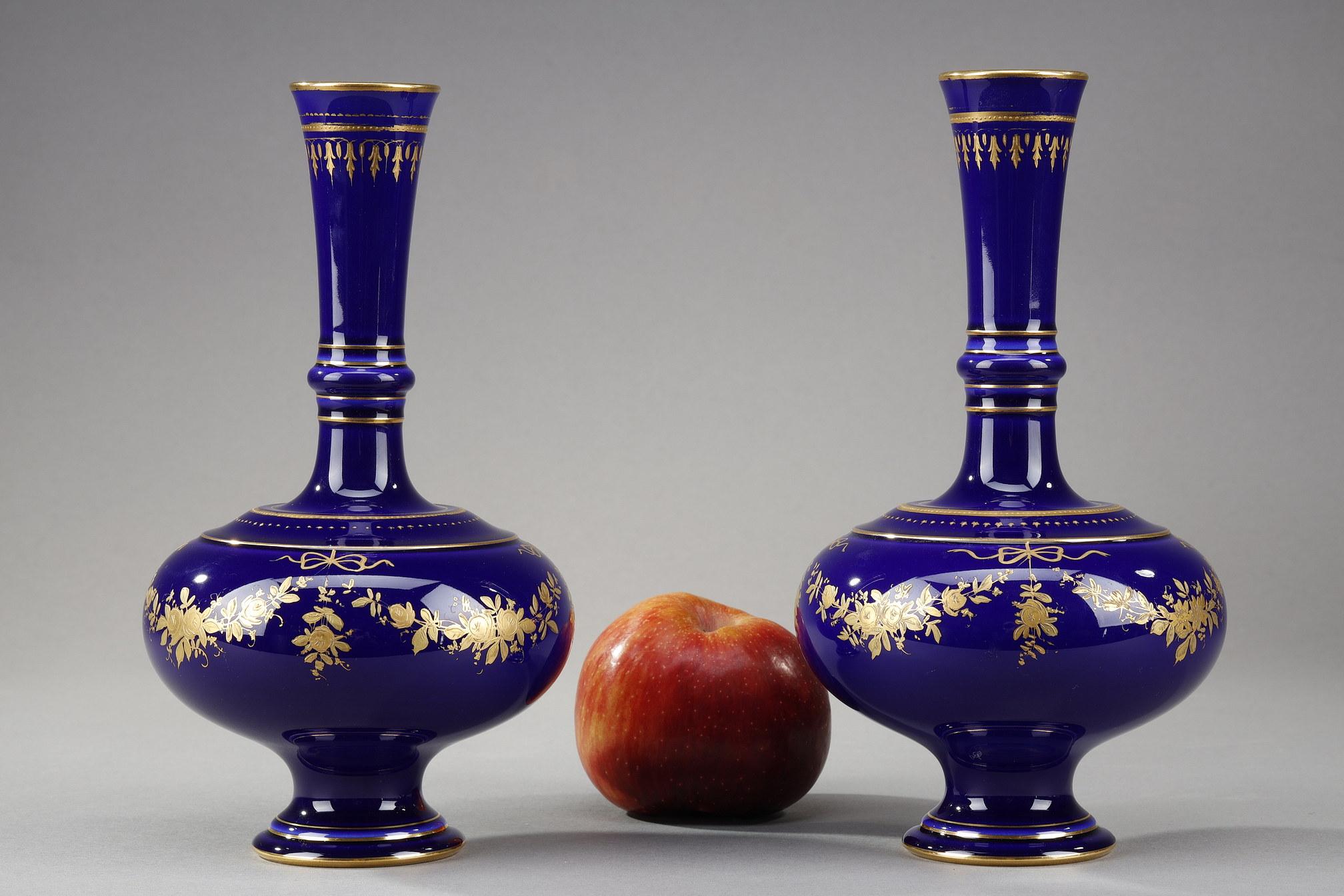 Pair of small vases with gilded decoration on a blue porcelain background. They have long necks with golden nets. Their bodies have a golden decoration is Louis XV style with garlands of flowers and decorative knot. It is a production of the