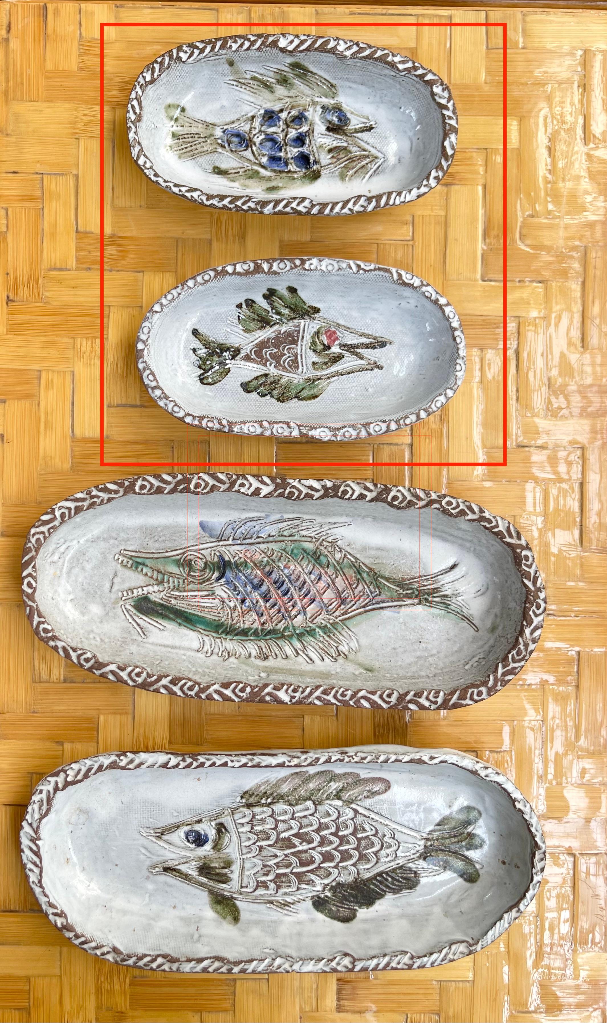 A pair of French ceramic decorative dishes with fish motif (circa 1970s) by Albert Thiry. Two oval-shaped ceramic dishes have a chalk-white glazed surface. Within the dishes' recesses a fish is incised into the glaze and painted in Thiry's trademark