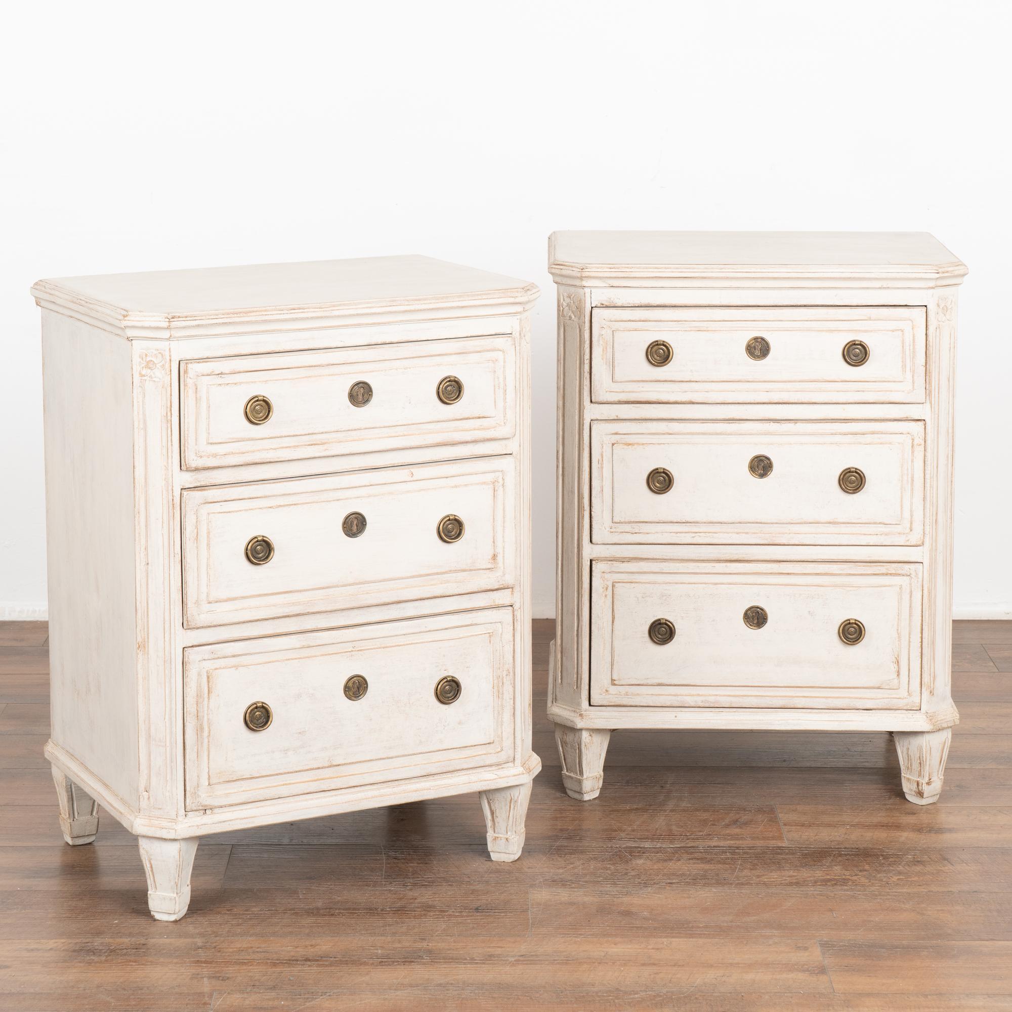 Pair, Gustavian style small pine chest of drawers with fluted canted sides and fluted tapered feet perfect to use as nightstands or small side tables. 
The three drawers each have two brass pulls to open.
The newer, professionally applied white