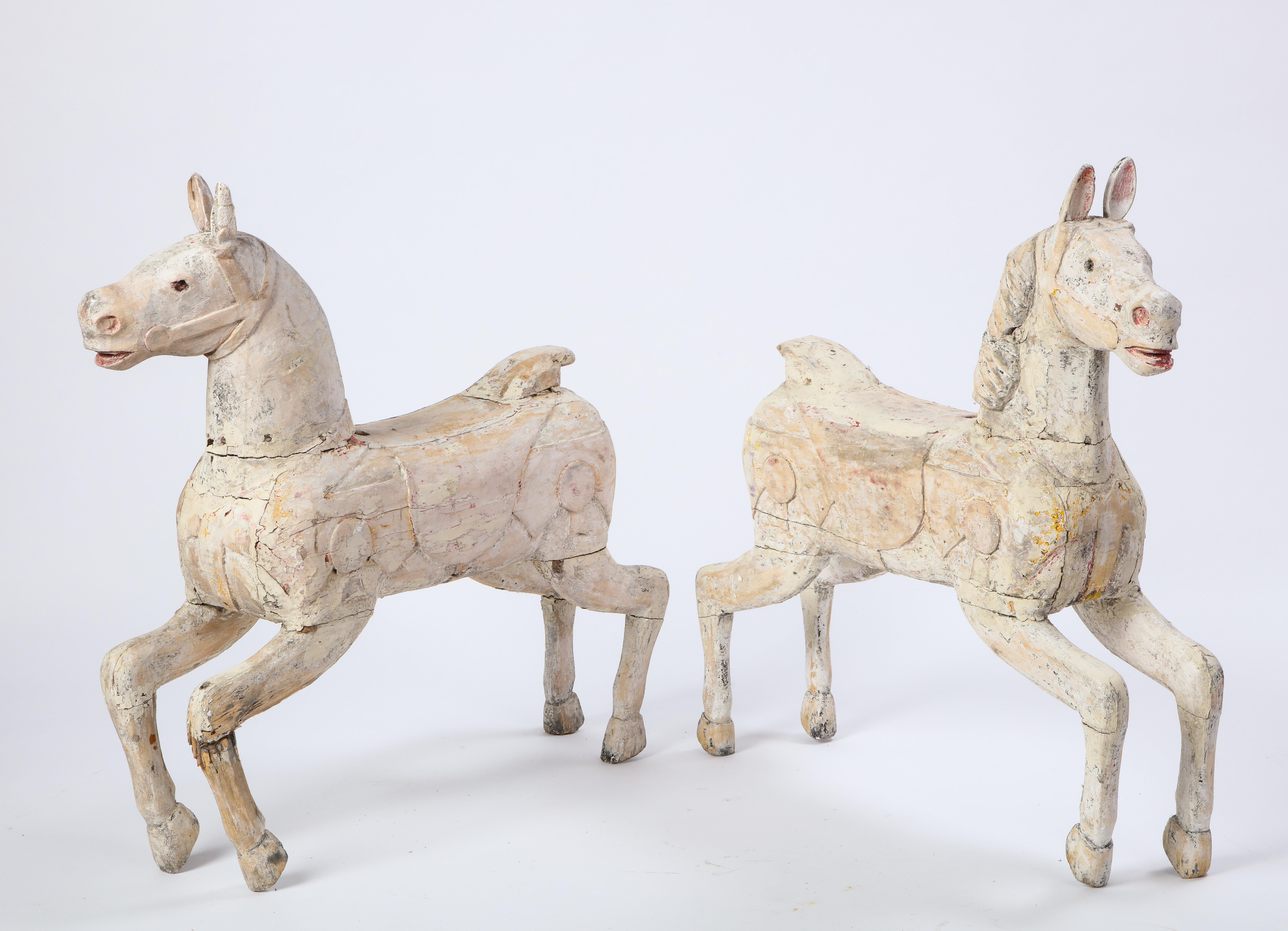 A pair of white-painted carved wood carousel horses from the 20th century. Each is modeled after a prancing horse, and measures H 33 in. x W 31.25 in. x D 8 in. The petite horses exude a playful quality and charm and the whitewashed surface adds