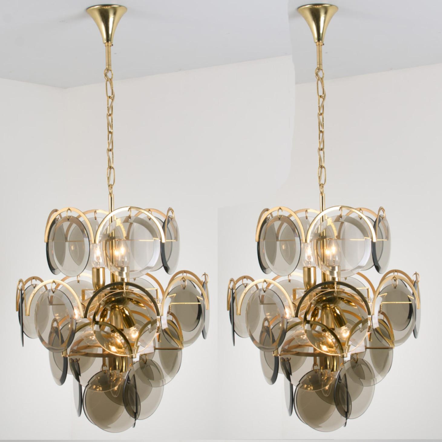 Pair of  gorgeous five tiers hanging light fixtures, in style of Vistosi. With graduated tiers of smoked round facet shaped glass discs framed by half-moon shaped brass. The chandeliers are complete, no hook or glass disk is missing with its