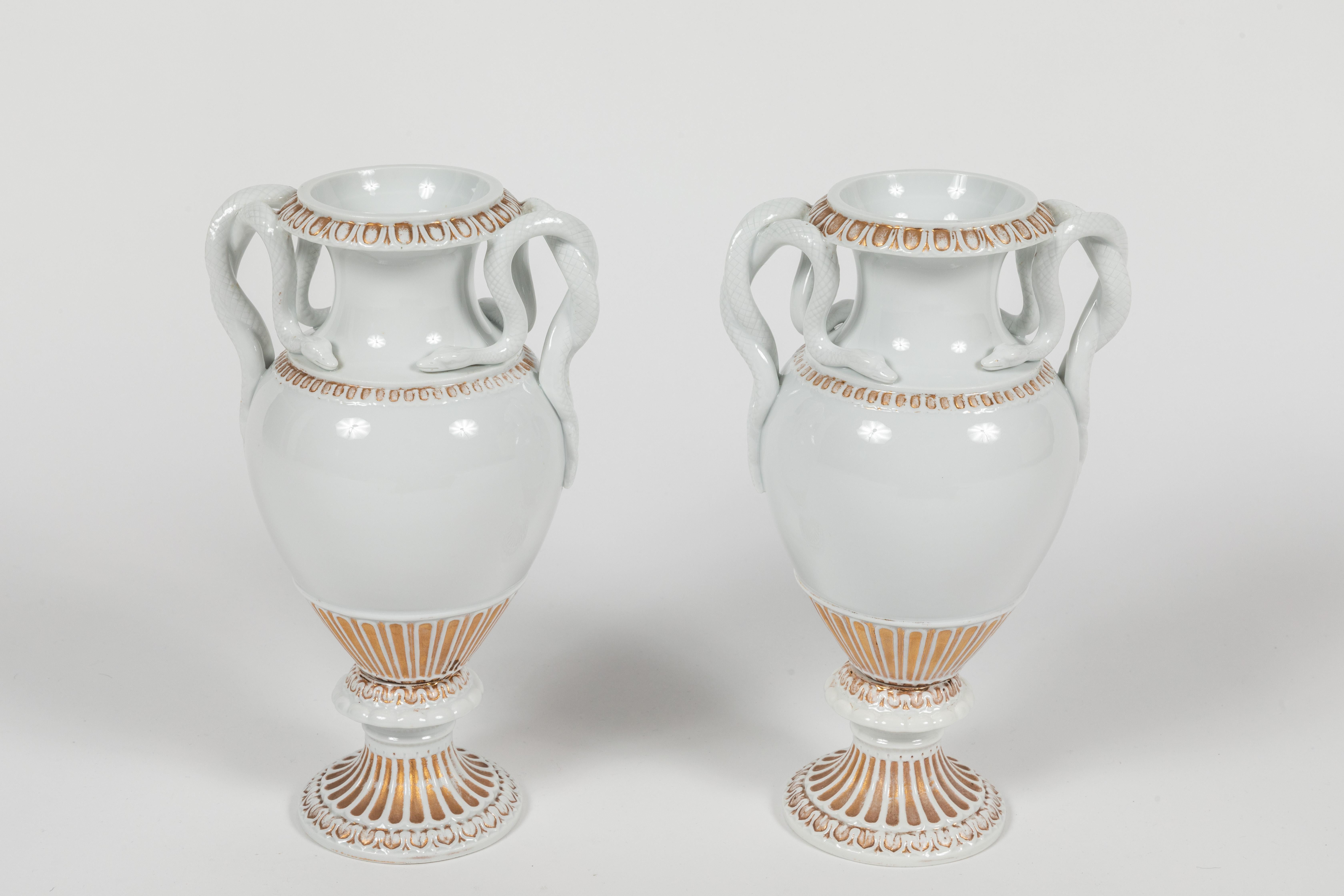 Stylish and chic pair of Meissen urns in Classic glazed white porcelain with gold accents. These urns are classical in form and feature entwined snakes as handles. A timeless design that works well in both Classic and contemporary interiors. The