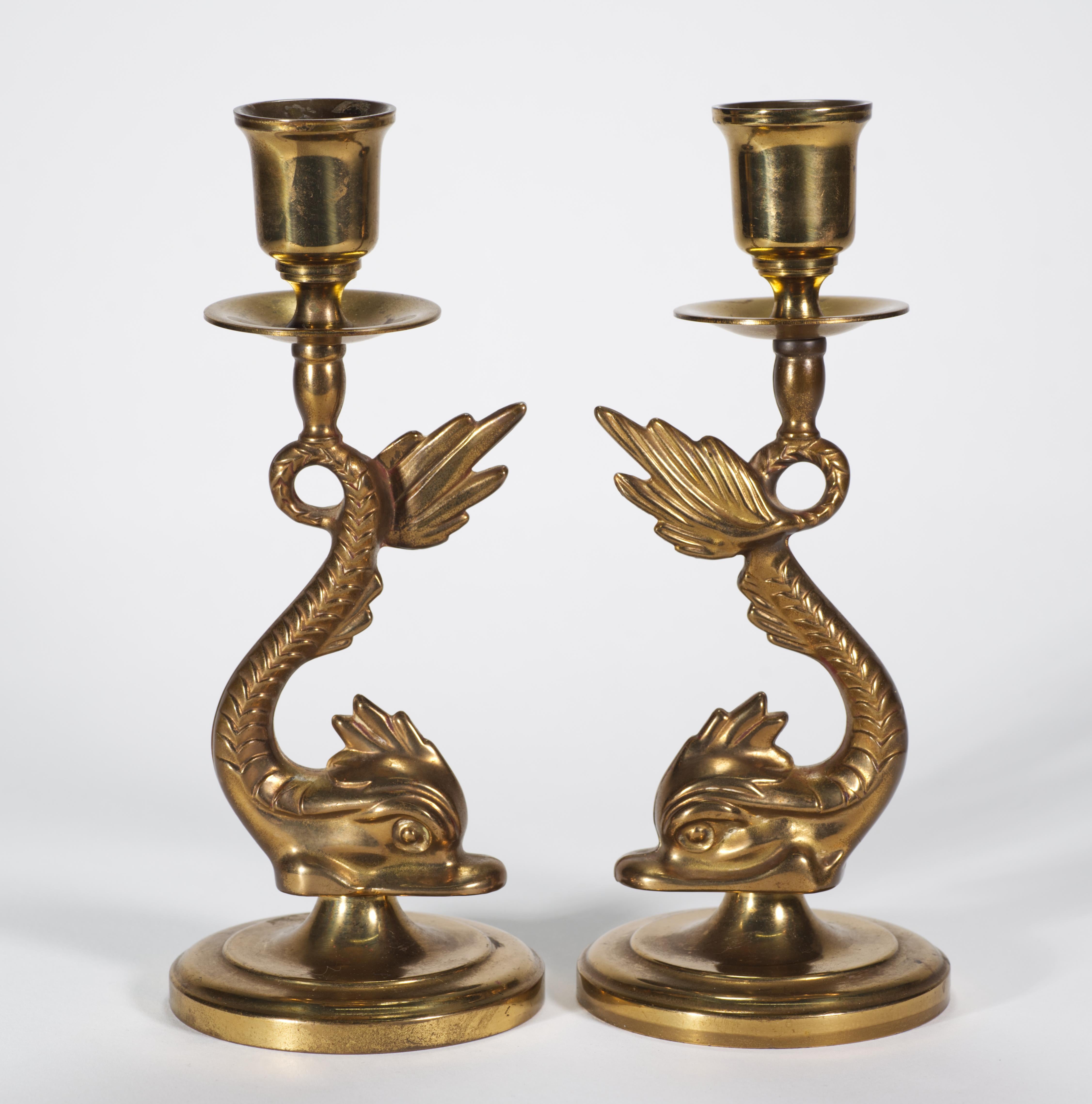 
Coppia di candelieri vintage in ottone massiccio con figure giocose di delfini che sostengono bobeches e portacandele con le loro code ricurve. Gli squisiti dettagli e la consistenza delle squame dei delfini sono accostati alla base rotonda dai