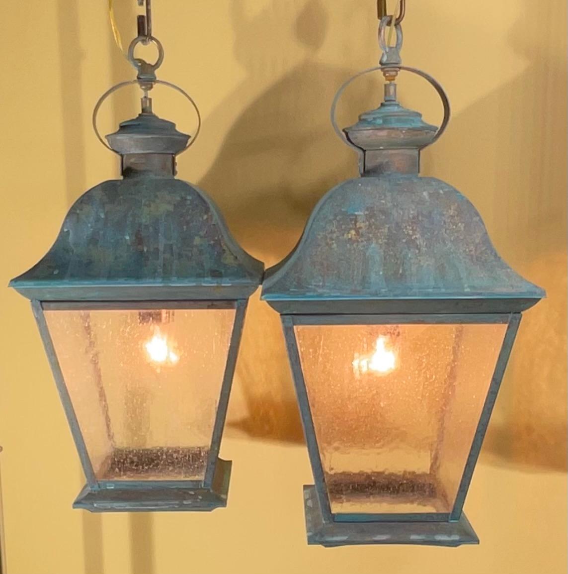 Elegant pair of solid brass hanging lanterns, exuding timeless charm and robust quality. These substantial lanterns boast a beautiful, verdigris patina, a testament to their enduring brass construction and exposure to the elements, adding a unique