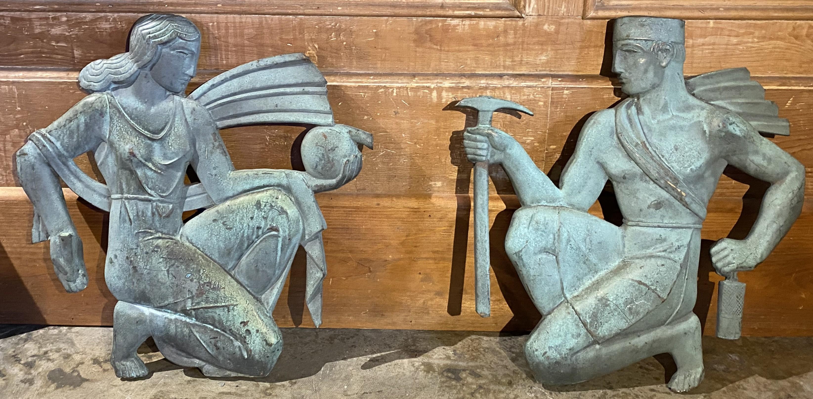 A fabulous pair of architectural Art Deco figures, probably solid bronze, the woman with a water jug, and the man with stonecutter’s tools, each with flowing robes behind them, loosely pin mounted to stone plinths. Purportedly acquired from a